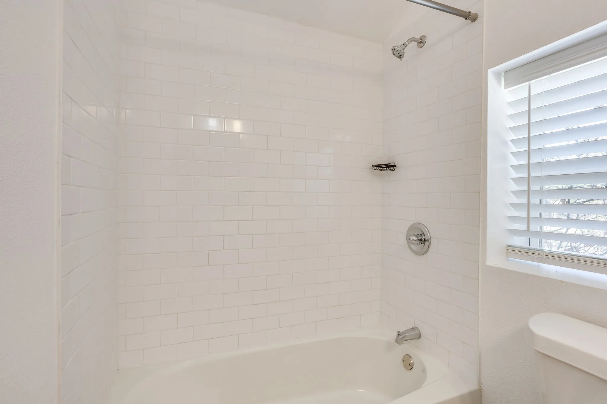 White subway tile surround, polished chrome fixtures, and a window with horizontal blinds