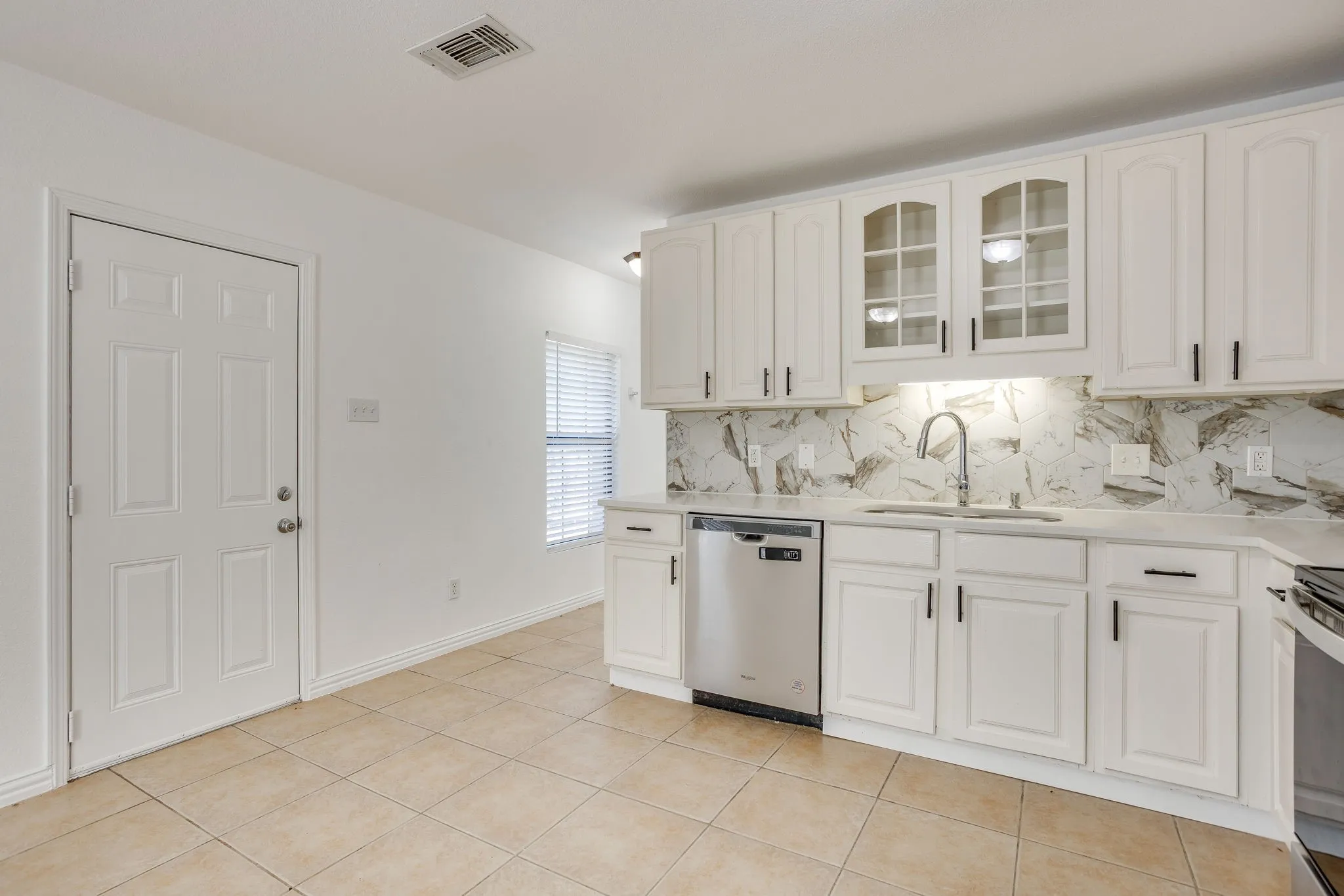 White cabinetry, stainless steel dishwasher, tile flooring, and a stone backsplash with coordinating countertops