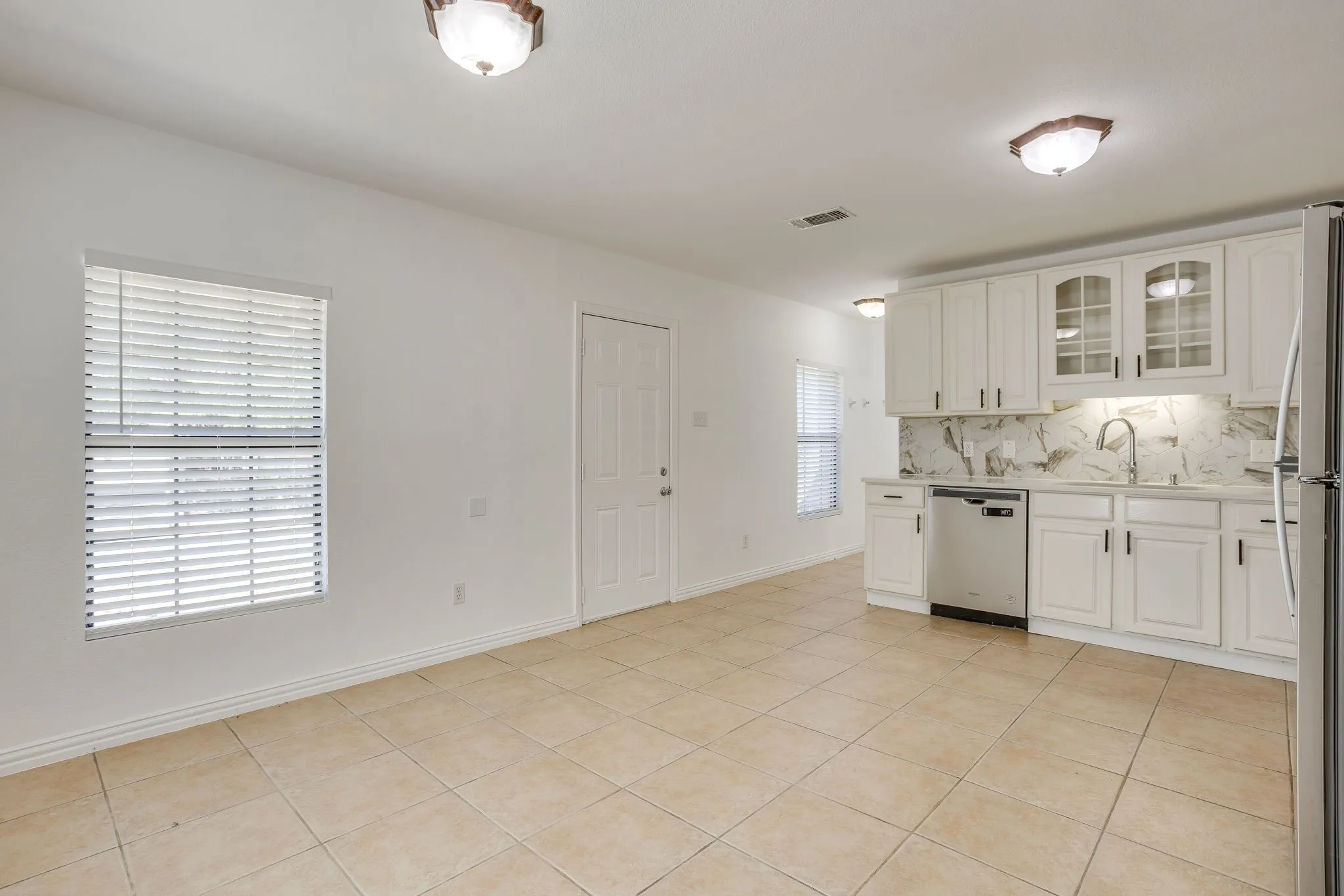 Kitchenette featuring white cabinetry, stainless steel dishwasher, undermount sink, and a stone-finish backsplash