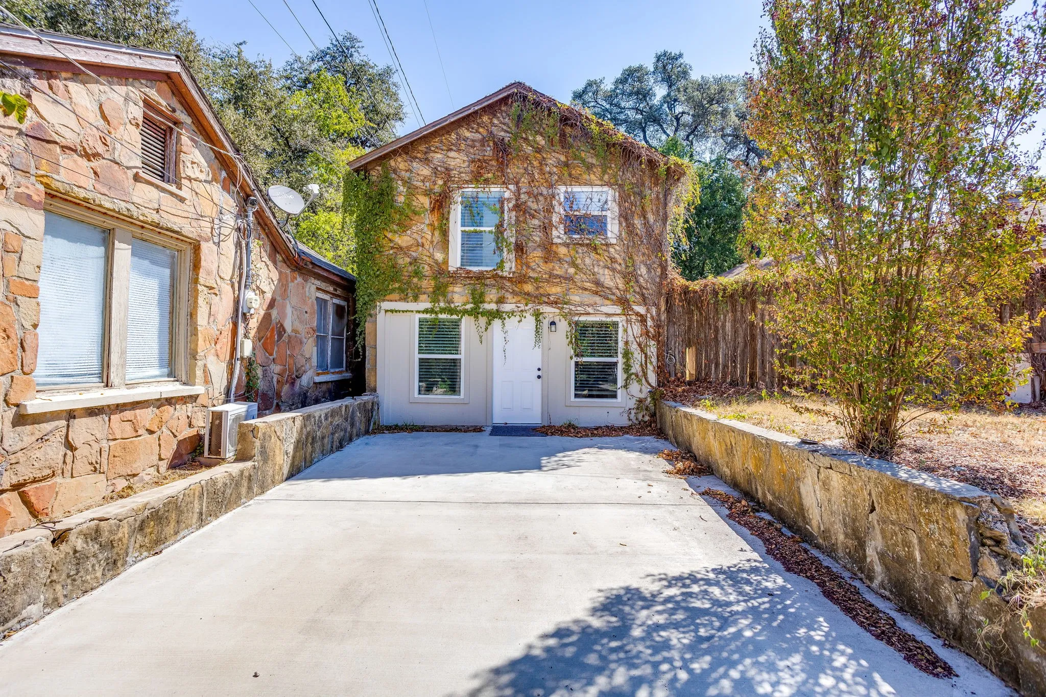 Stone veneer facade, concrete driveway, mature landscaping, retaining wall