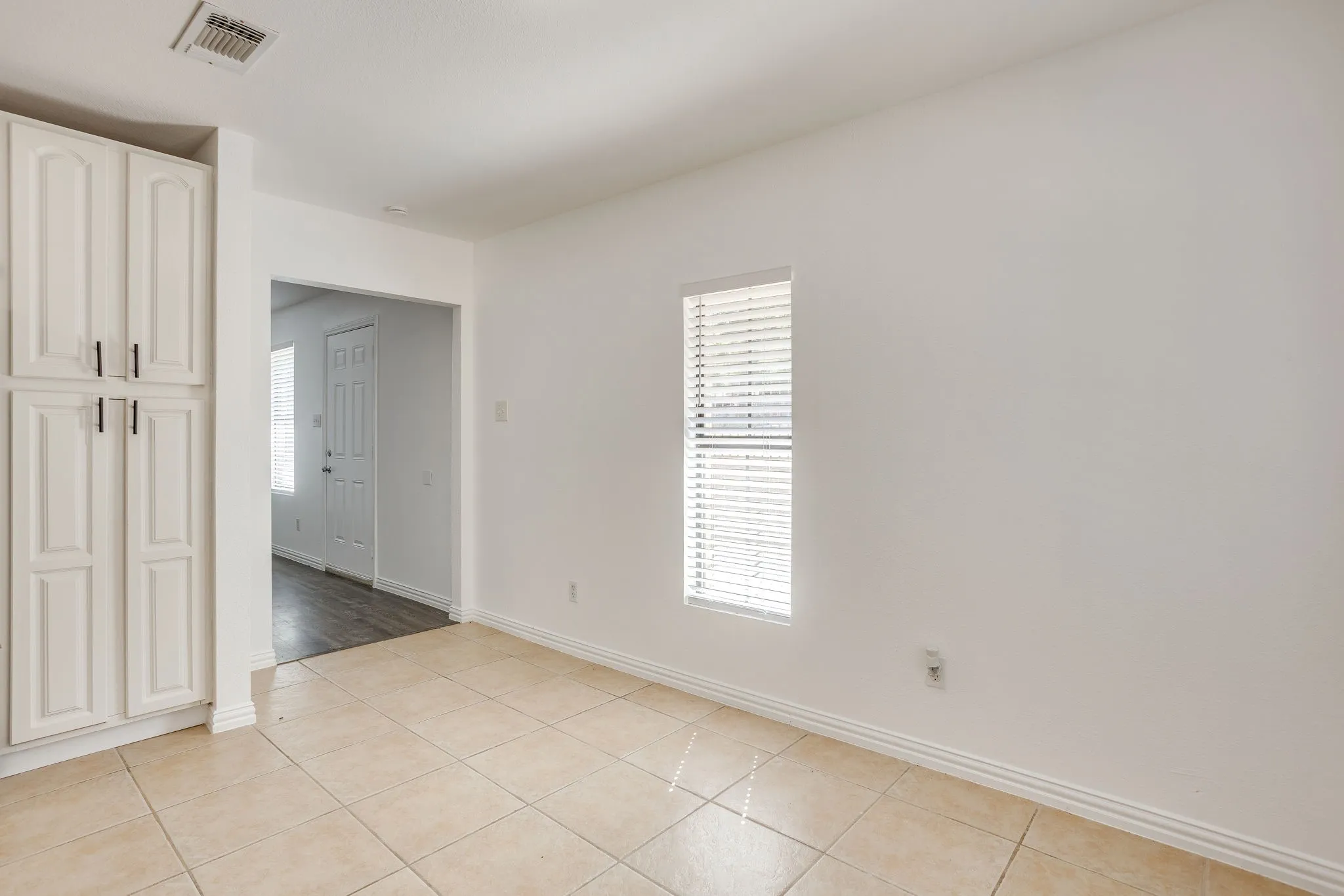 Neutral tone walls with a single window featuring blinds, complemented by tiled flooring