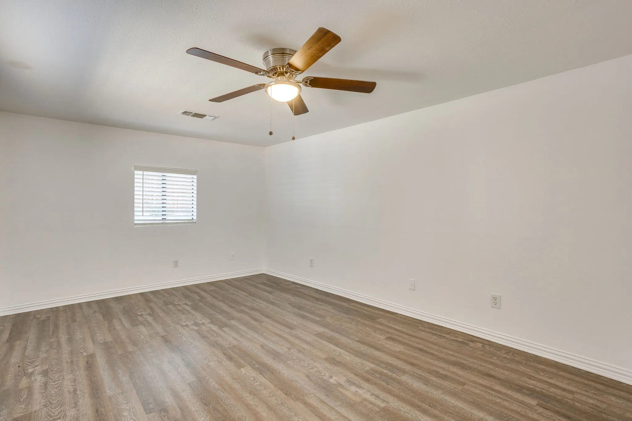 Spacious room featuring wood-finish flooring, white walls, and a ceiling fan with integrated lighting