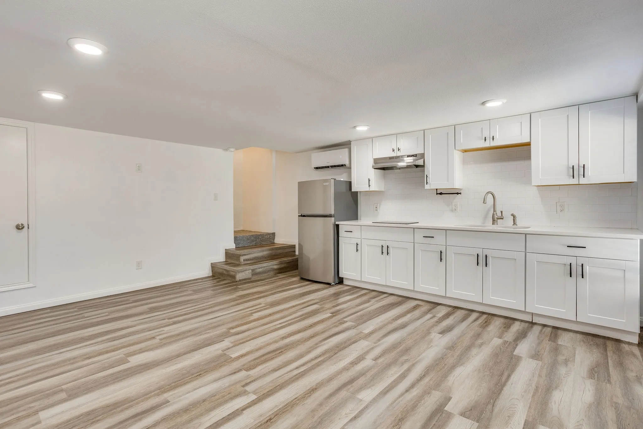 White shaker cabinetry, light-toned countertops, subway tile backsplash, stainless steel refrigerator, and wood-finish flooring