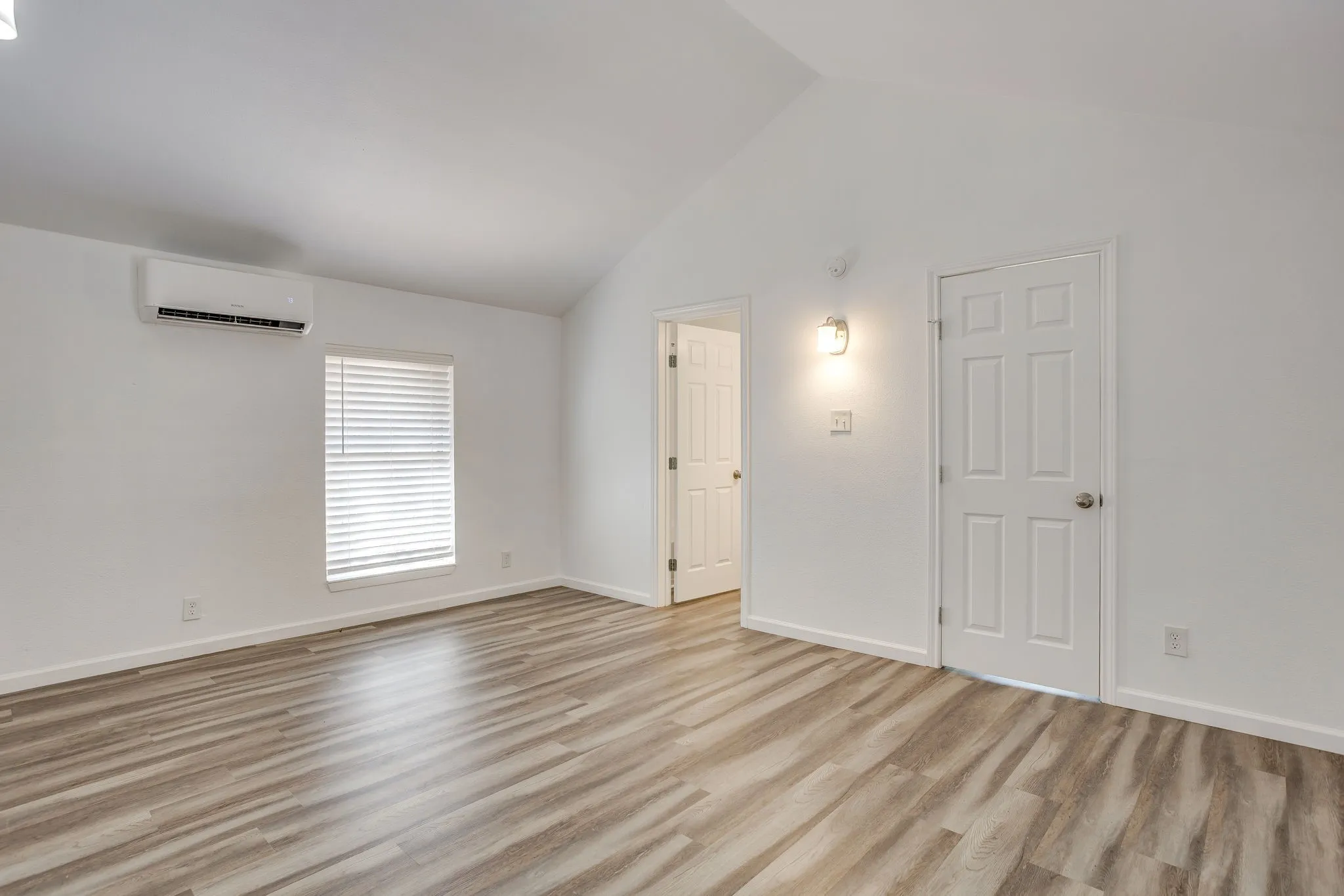 Vaulted ceiling overhead, wood-finish flooring, white walls, and a window with blinds