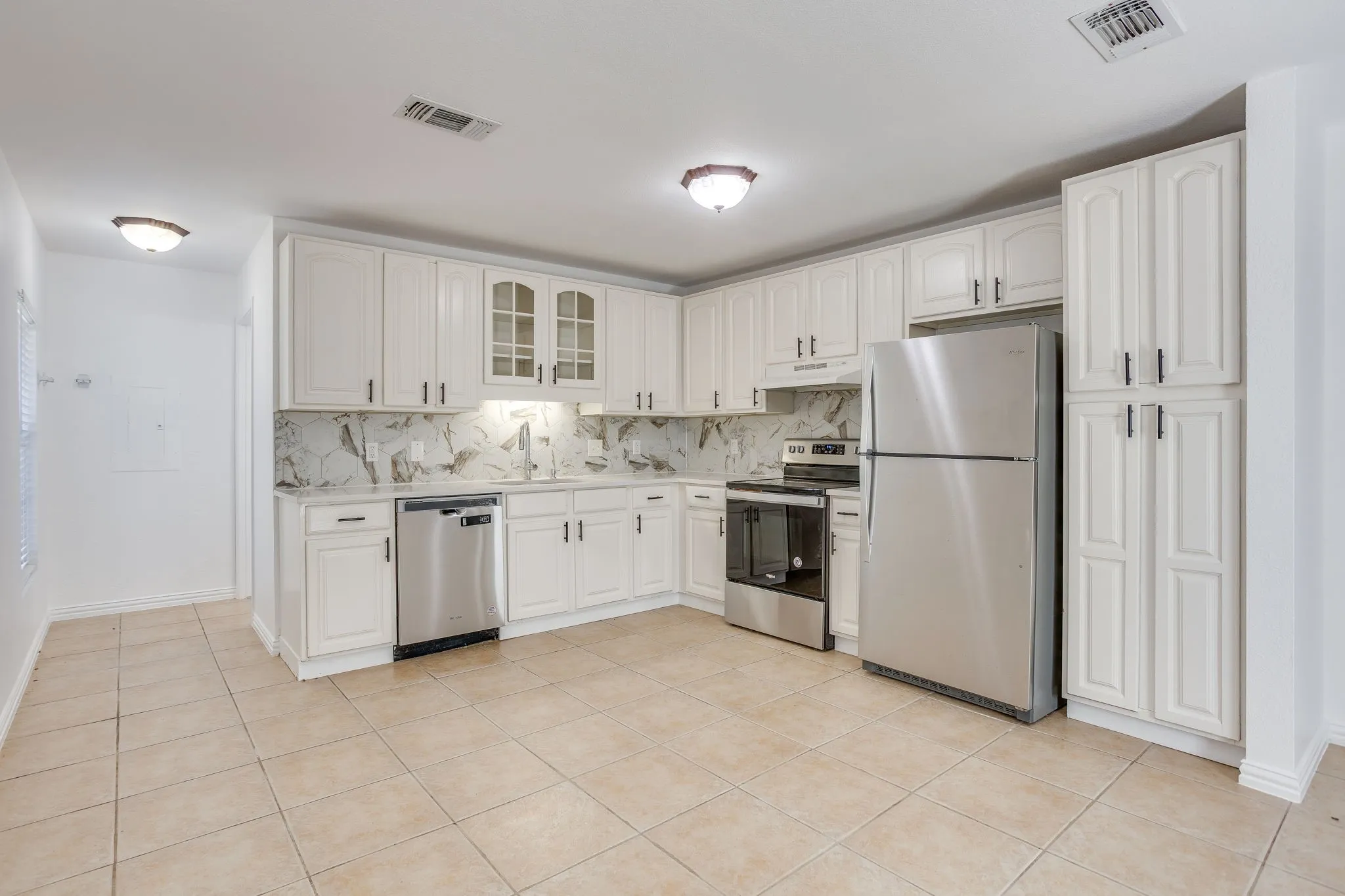 Kitchen featuring white cabinetry, stainless steel appliances, tile flooring, and a stone-finish backsplash