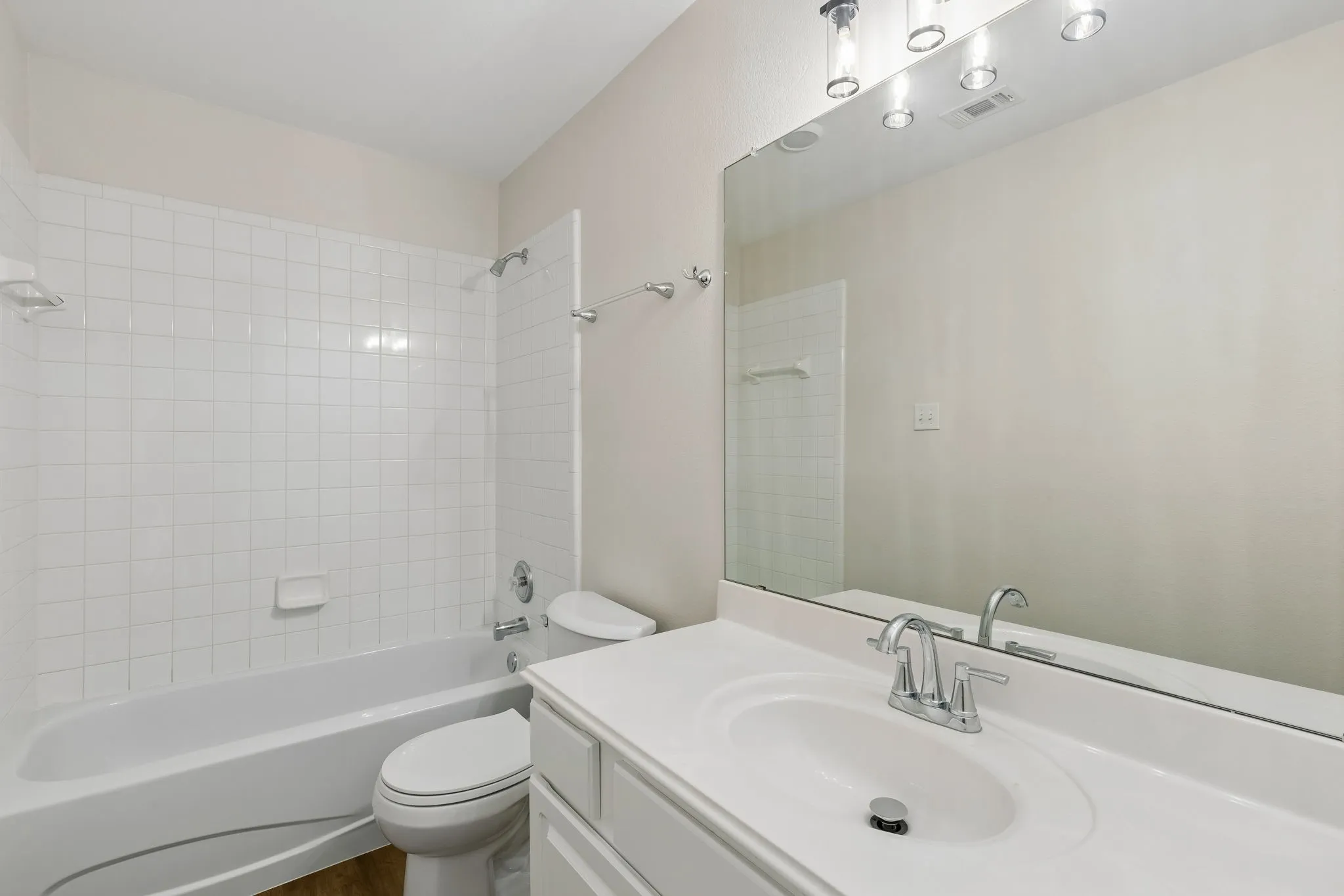 White ceramic tile shower surround, single vanity with integrated sink, chrome faucet, wall-mounted mirror, and brushed nickel light fixture