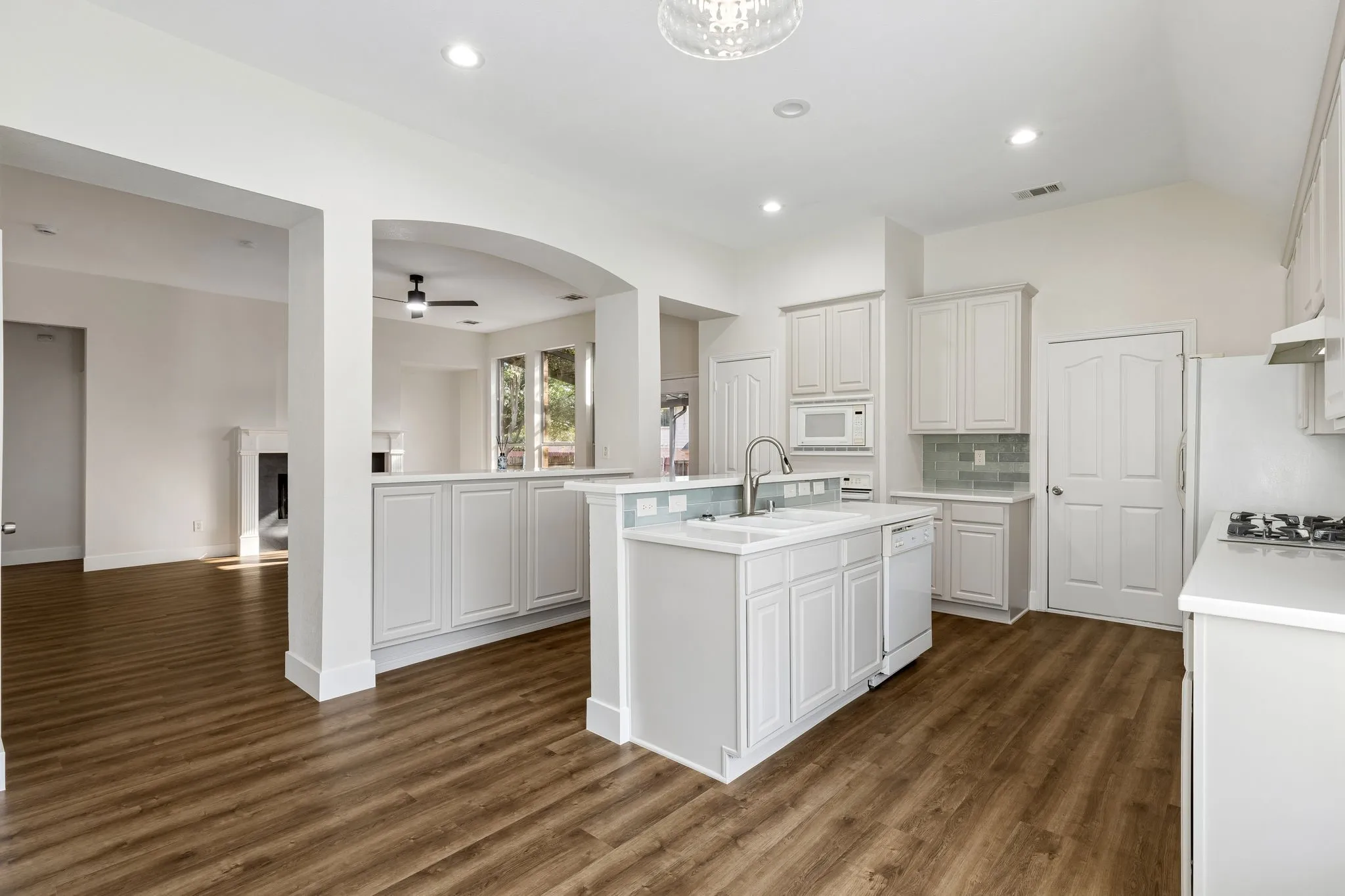 Bright kitchen featuring a central island with a double basin sink, white cabinetry, integrated microwave, and wood-finish flooring