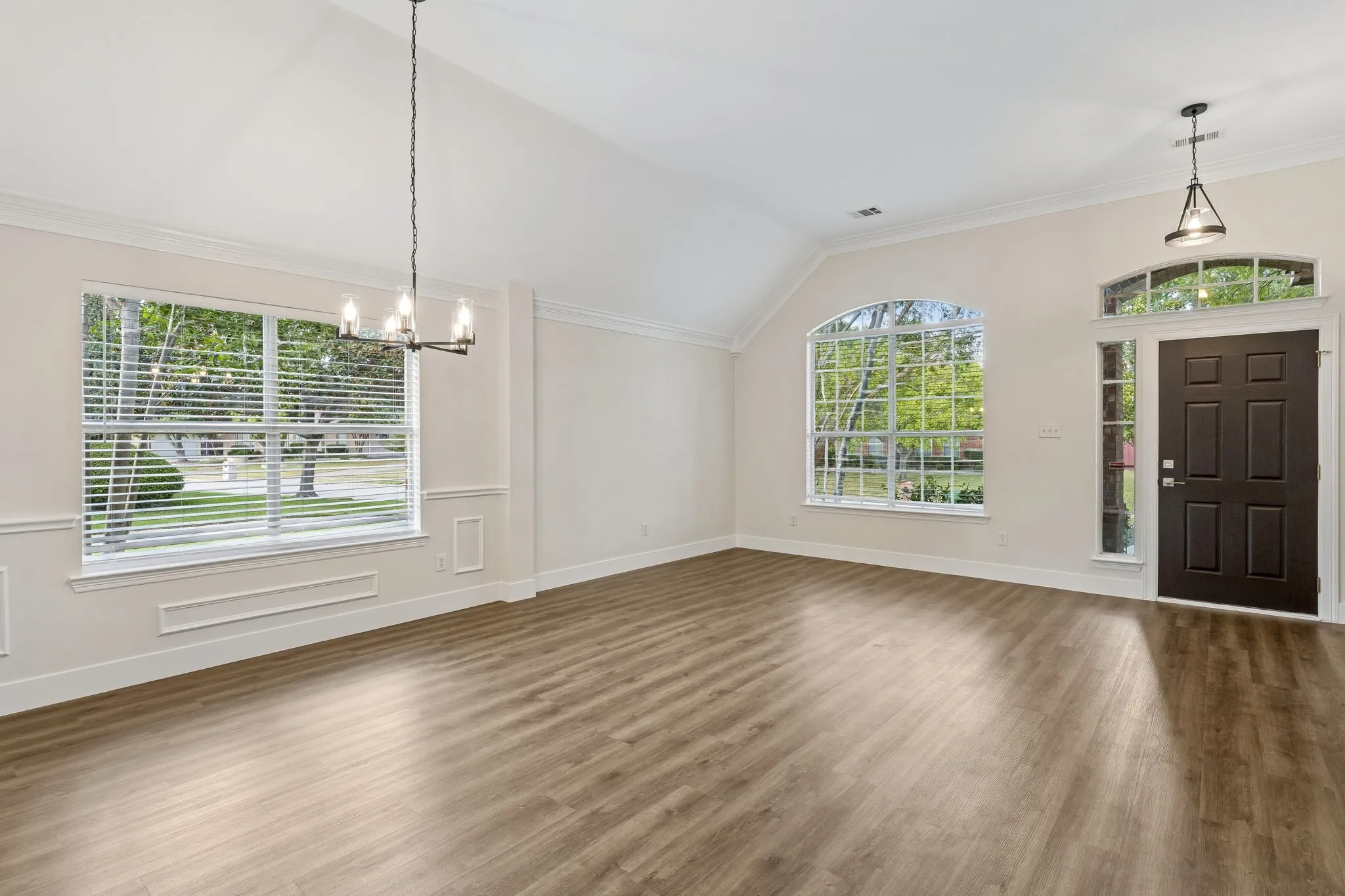 Vaulted ceiling with an attached chandelier, wood-finish flooring, and a paneled entry door with sidelights and an arched transom window