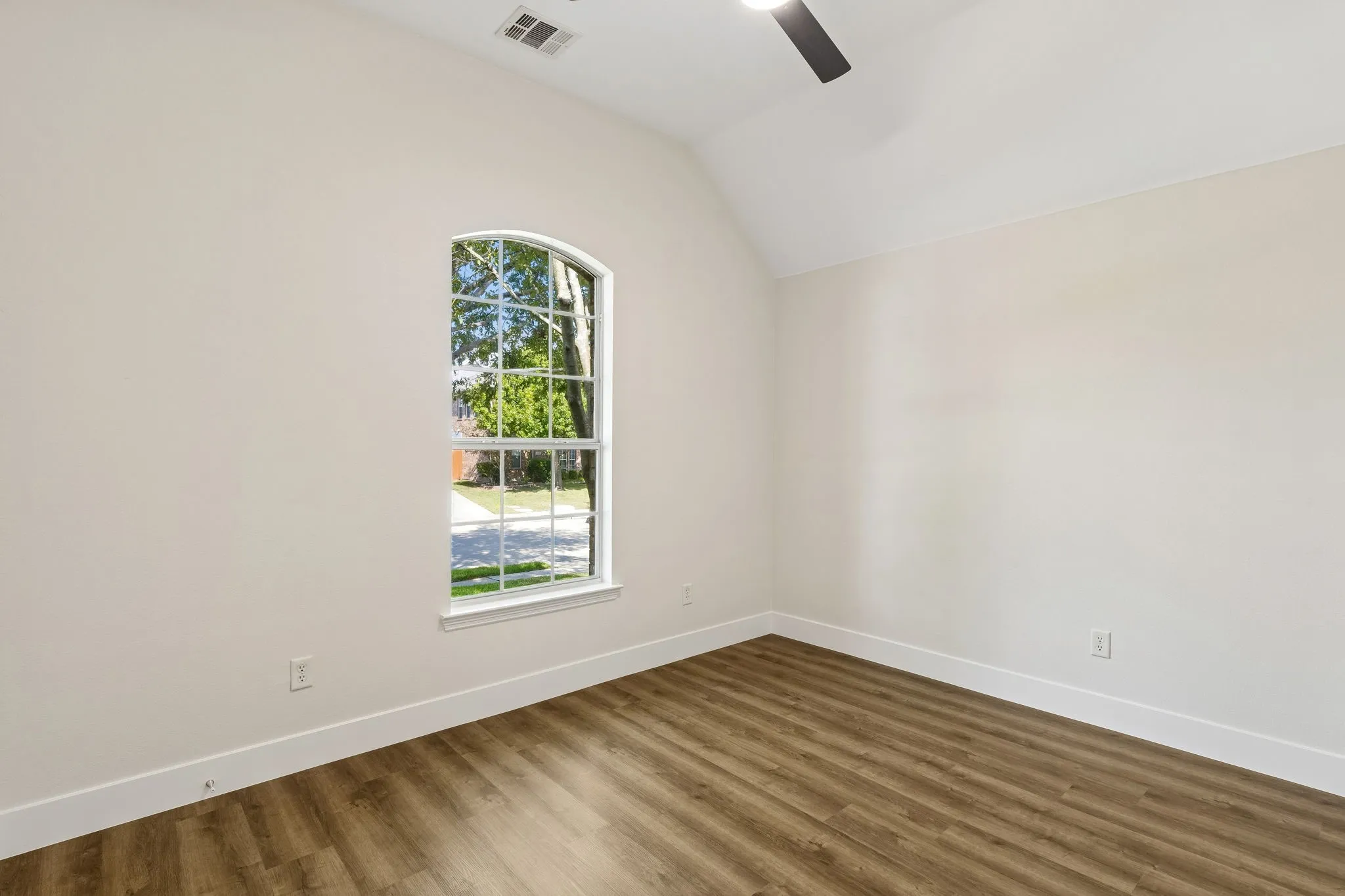 Vaulted ceiling with a ceiling fan, arched window with grid, and wood-finish flooring