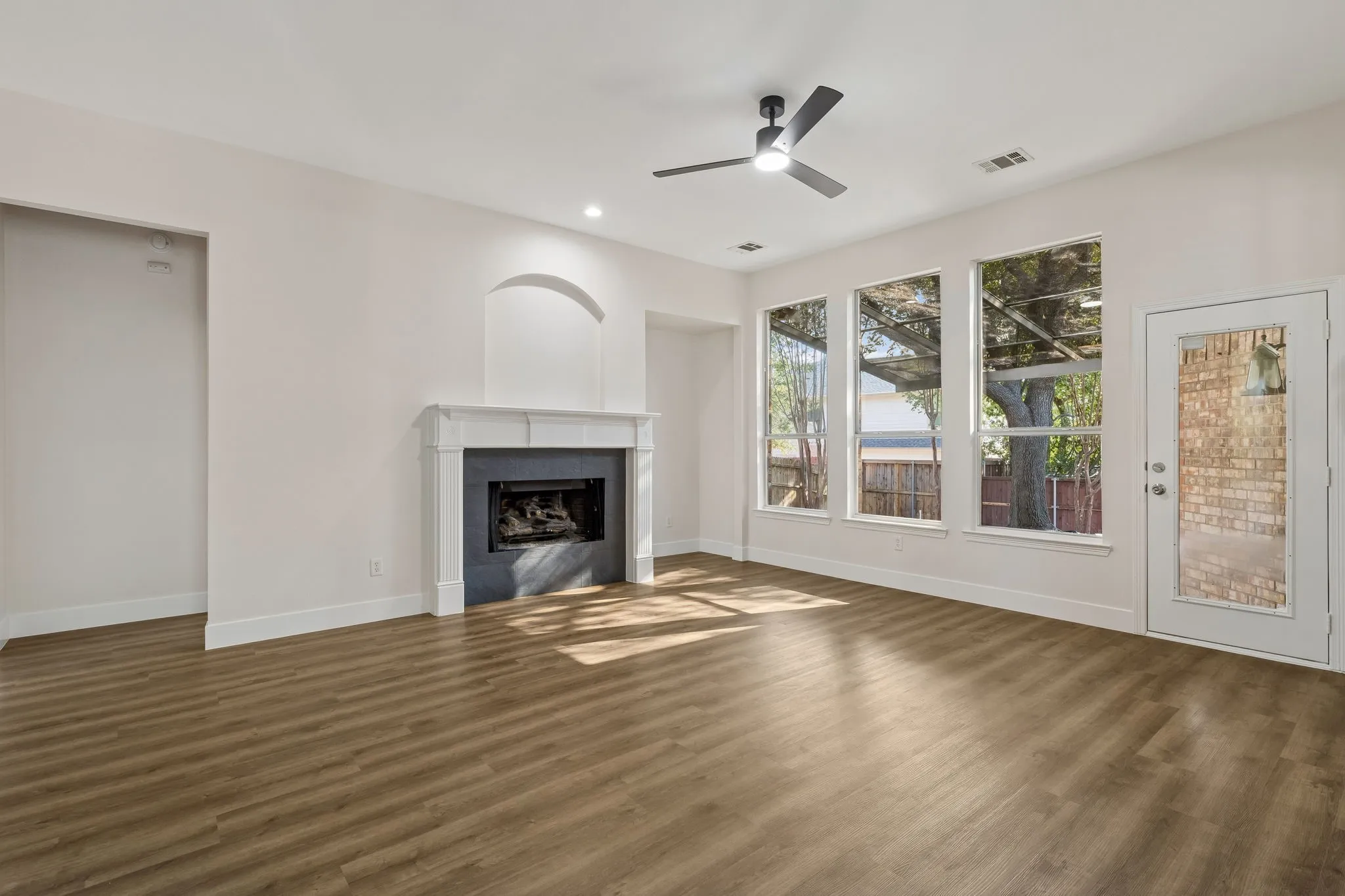 Spacious living area featuring wood-finish flooring, a contemporary ceiling fan, and a fireplace with a white mantel and dark stone surround