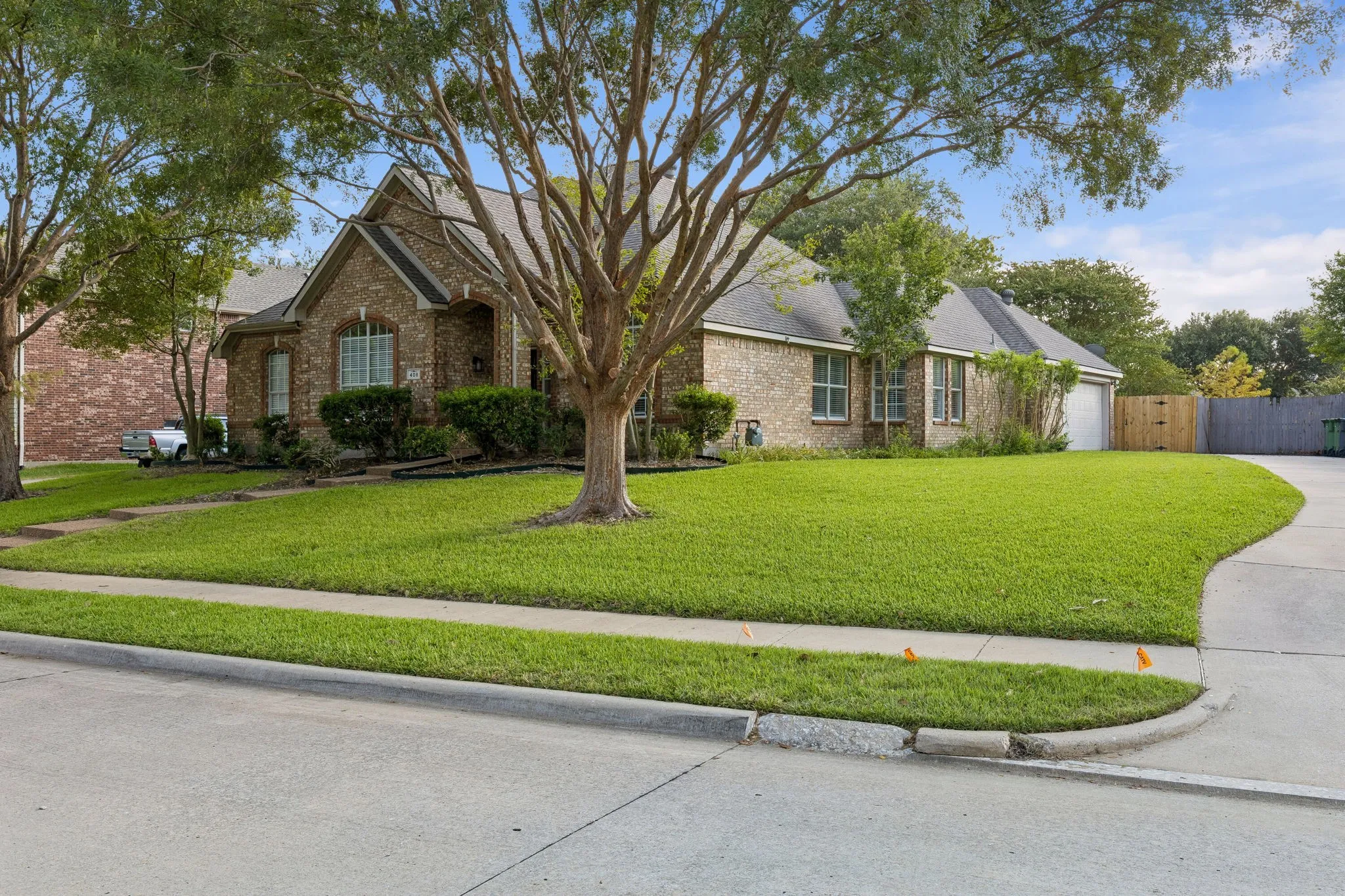 Brick exterior, gabled roofline, mature trees, expansive lawn, concrete driveway