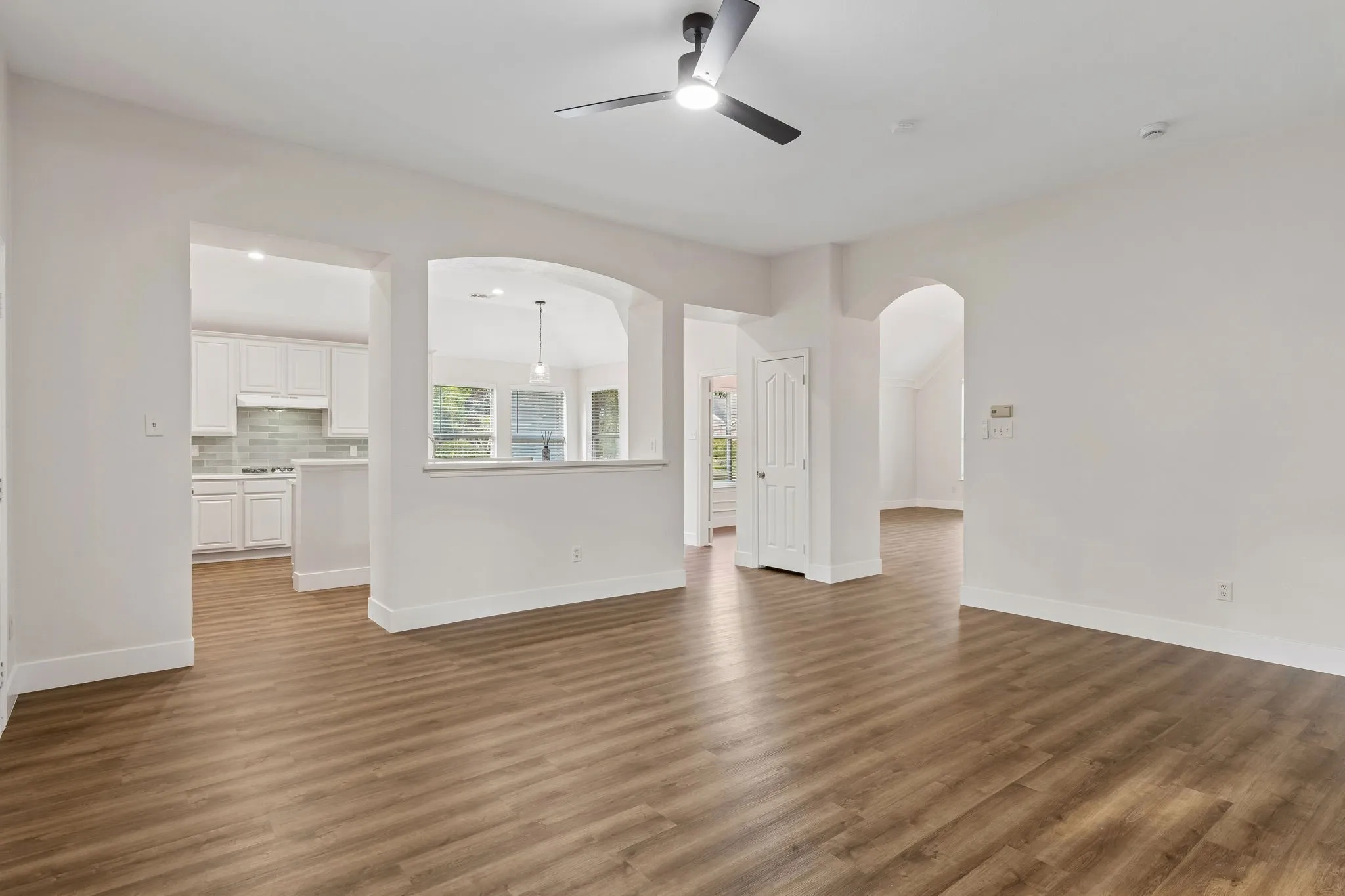 Open living area featuring wood-finish flooring, white walls, and a ceiling fan with integrated lighting