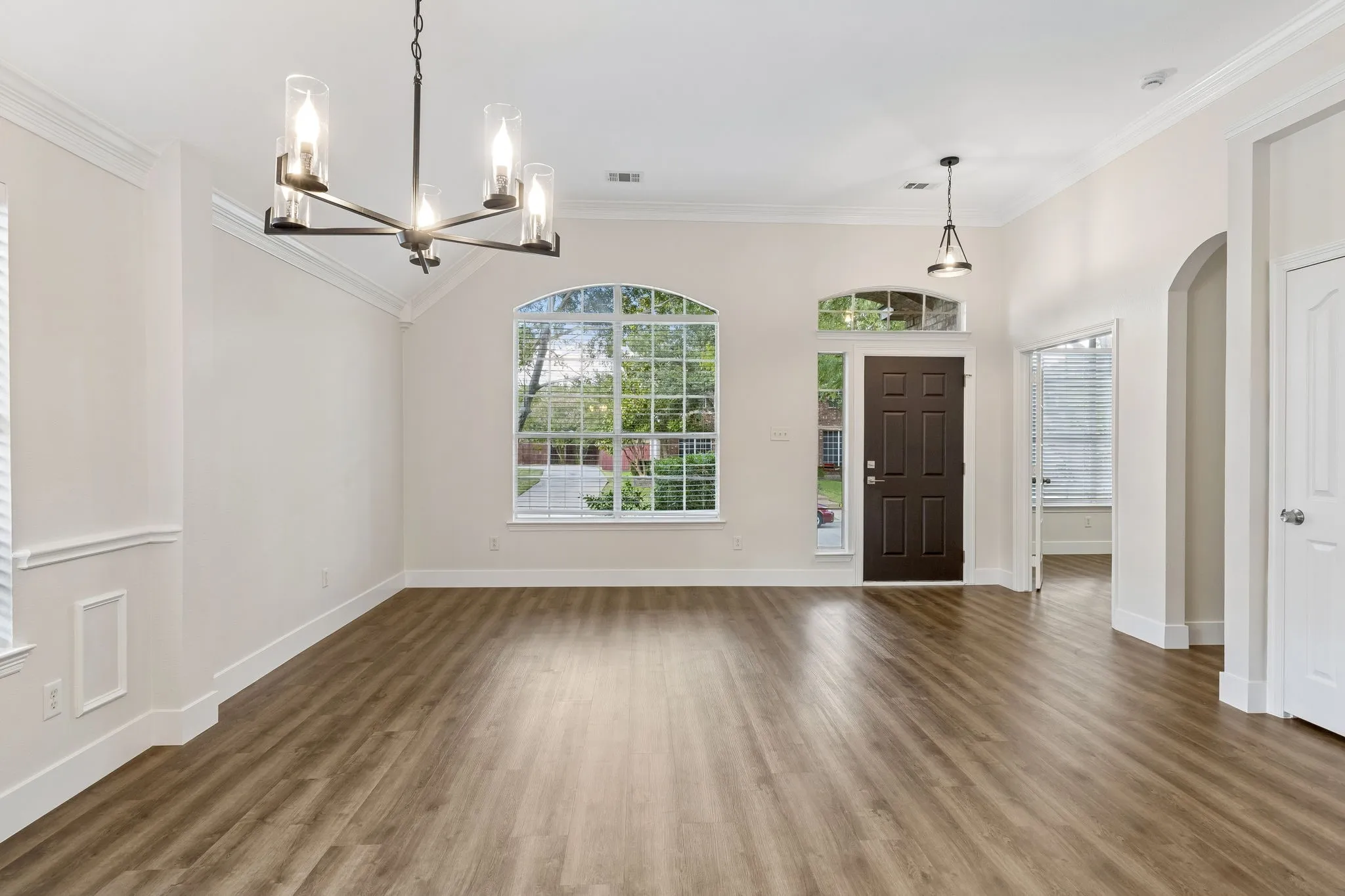 Vaulted ceiling with crown molding, wood-finish flooring, arched windows, modern chandelier, and dark wood-paneled door