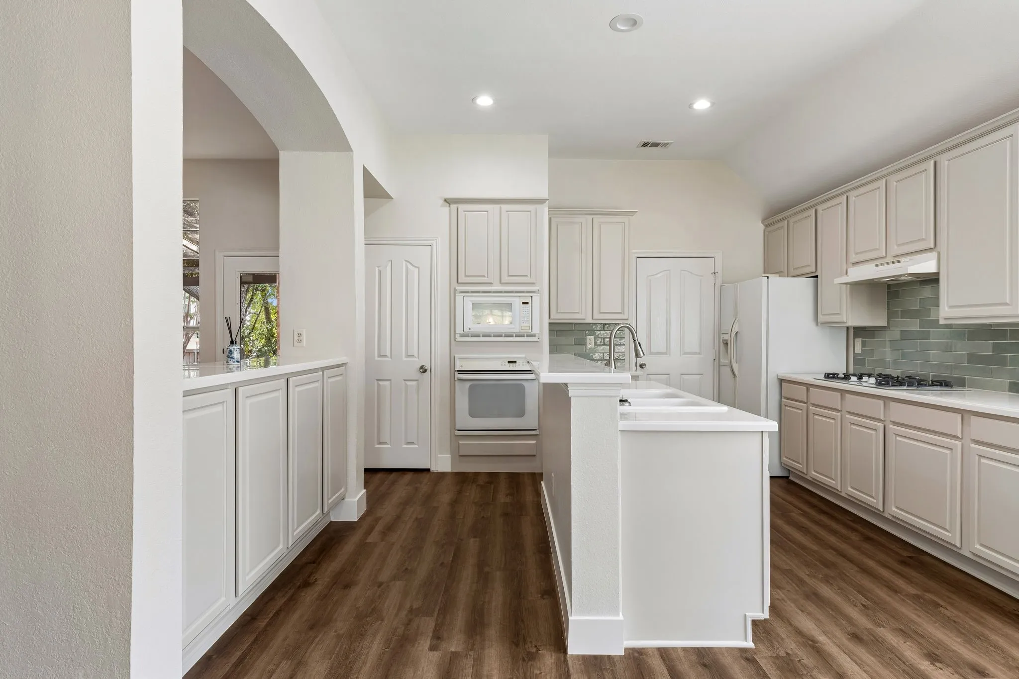Kitchen featuring a central island, wood-finish flooring, recessed lighting, white cabinetry, and a glass tile backsplash