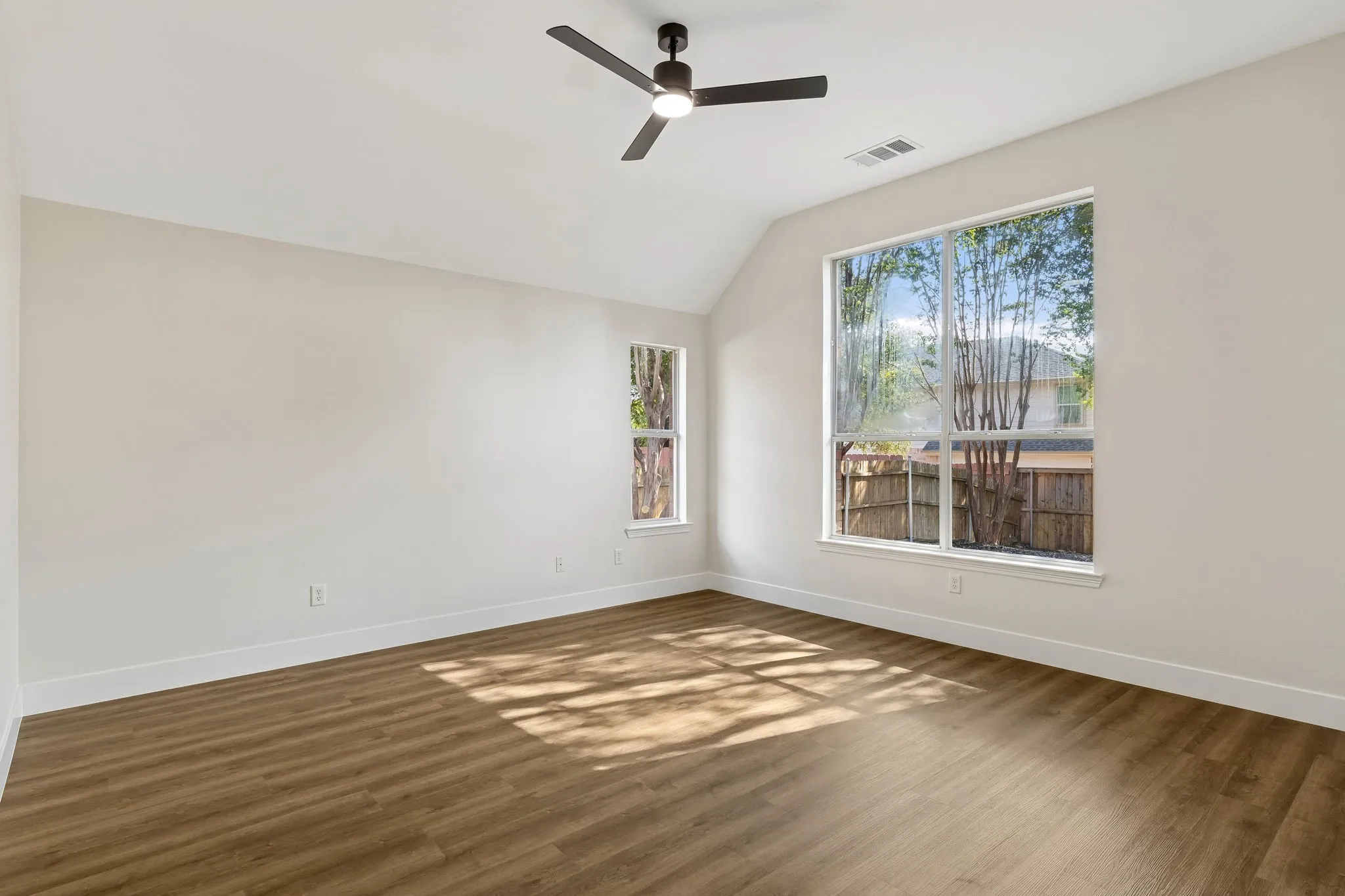 Vaulted ceiling, wood-finish flooring, ceiling fan, large windows, and neutral wall tones