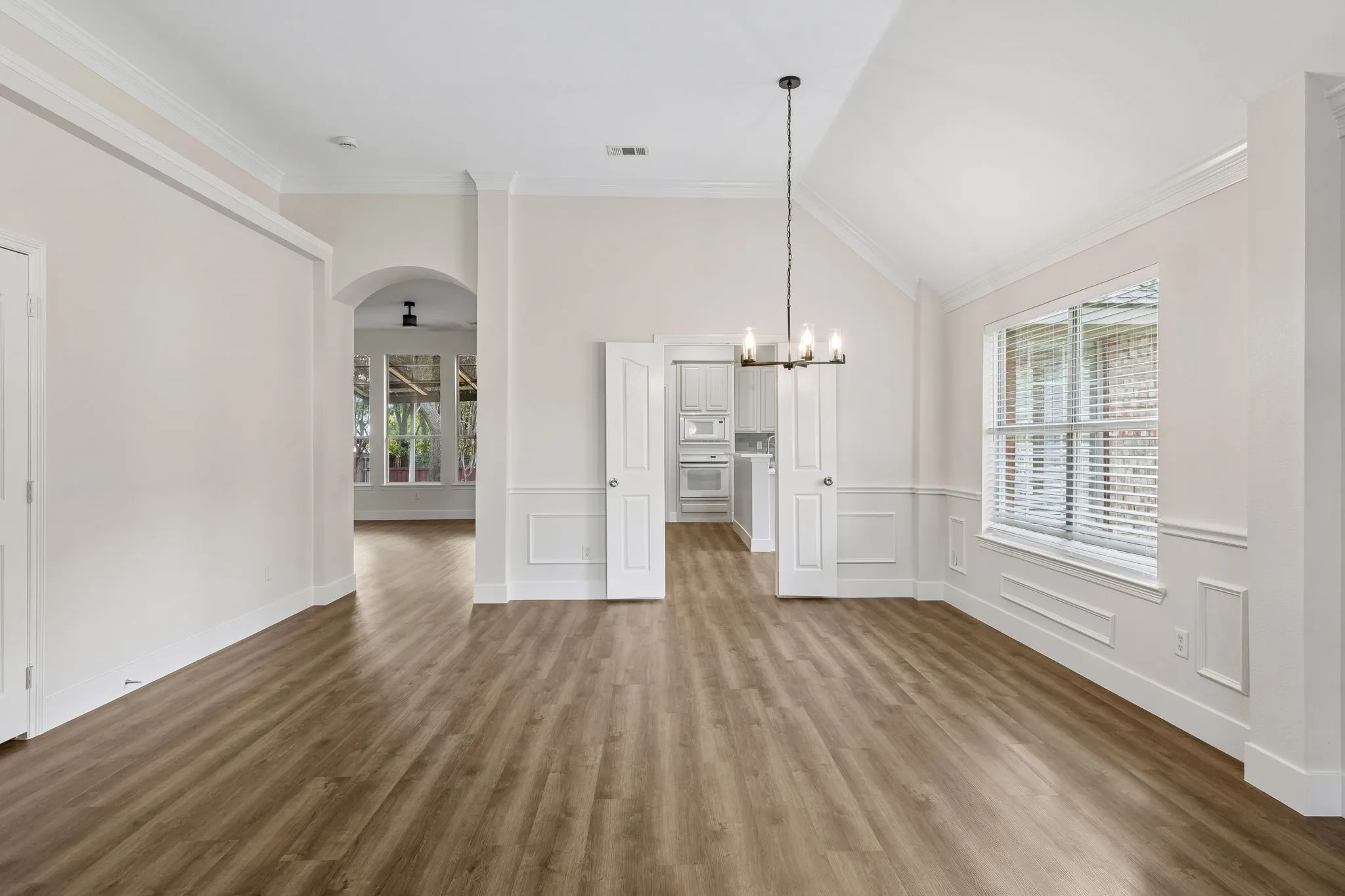 Wood-finish flooring, vaulted ceiling, crown molding, chair rail with panel molding, and an arched doorway