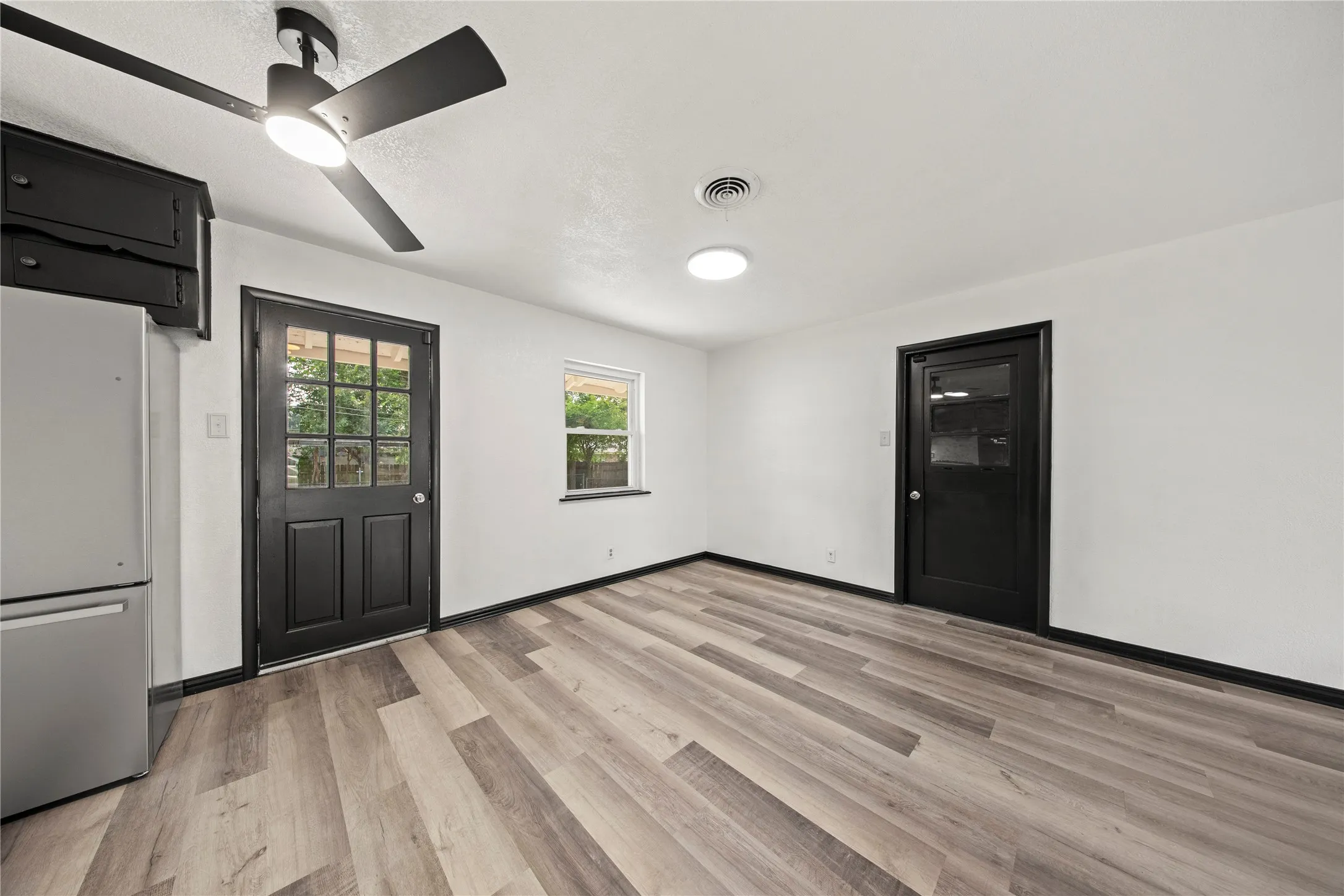 Wood-finish flooring, white walls, black trim, and a ceiling fan with integrated lighting