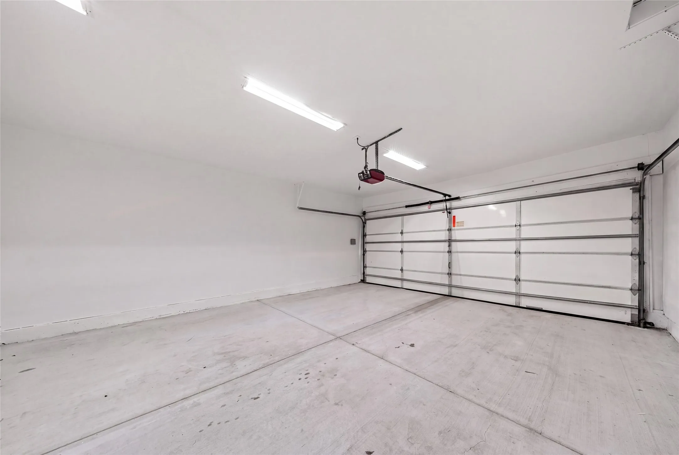 Spacious garage featuring a concrete floor, bright overhead strip lighting, and an automatic garage door opener