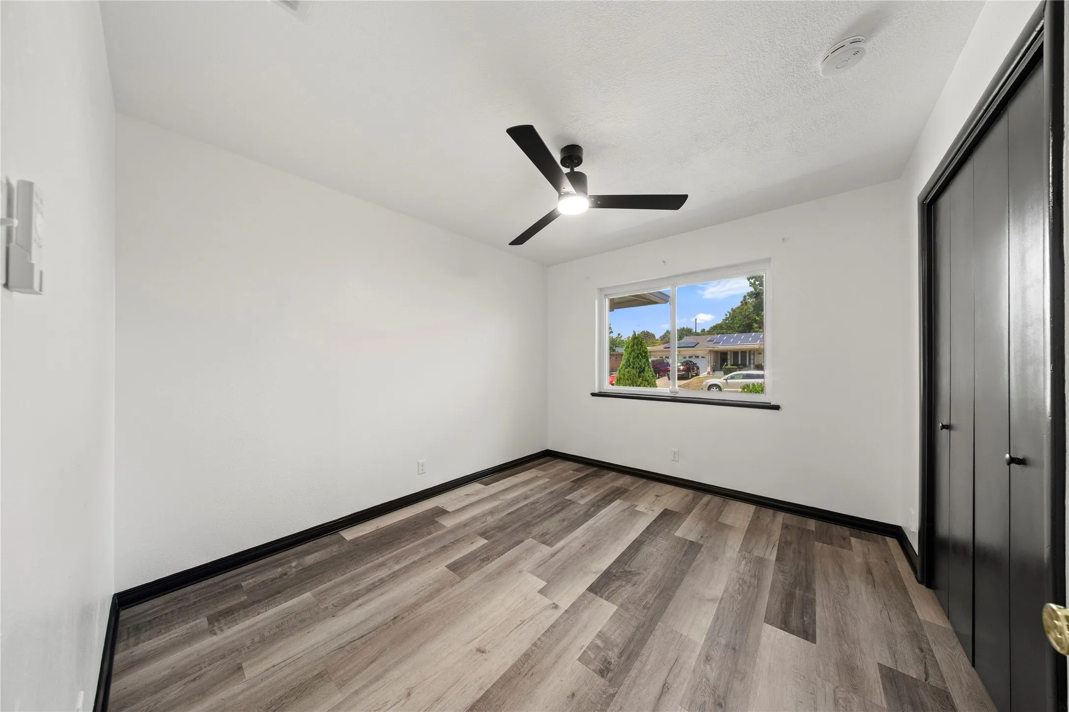 Wood-finish flooring, white walls, and a black ceiling fan with integrated lighting