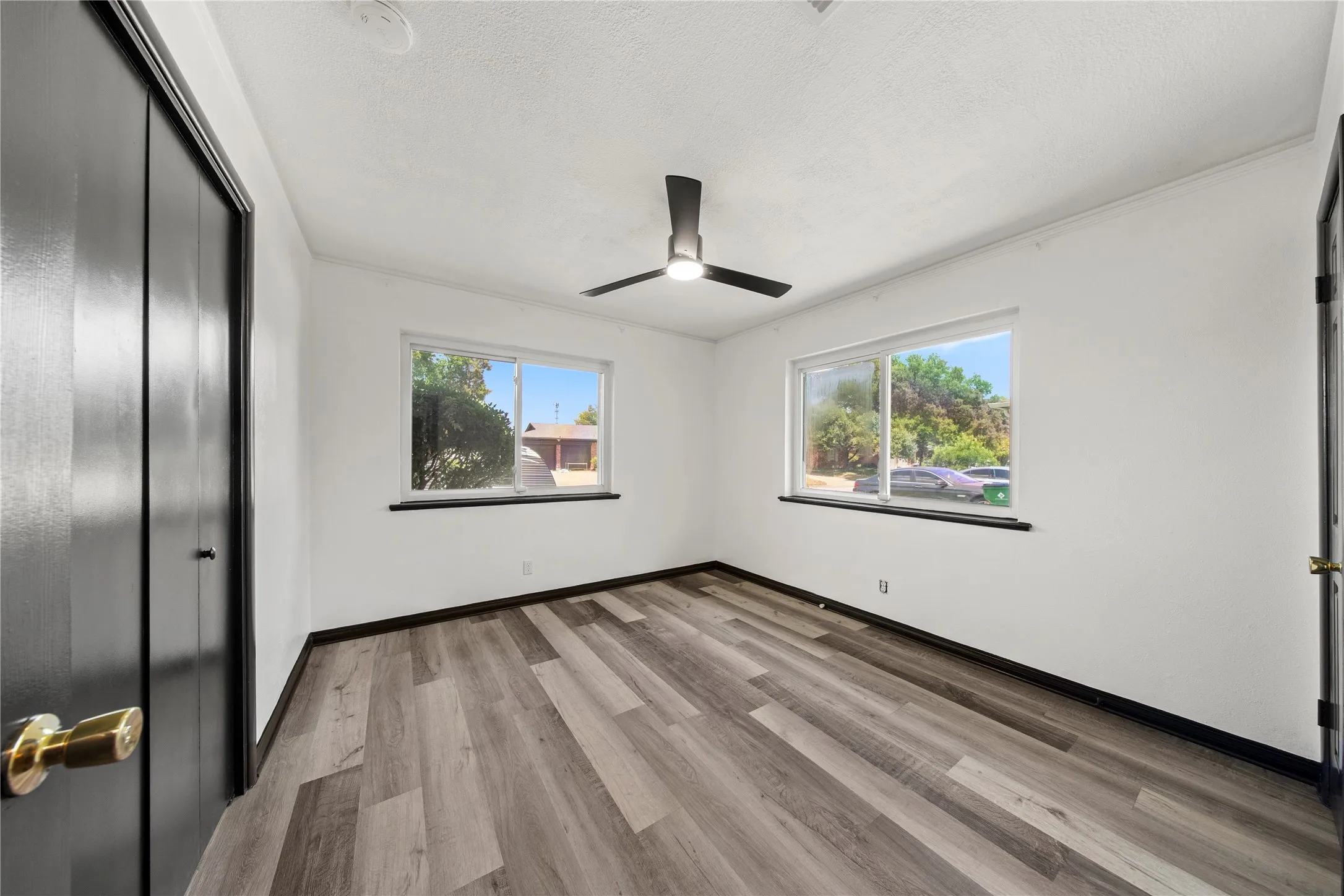 Wood-finish flooring, two large windows, black ceiling fan with integrated lighting, and a closet with bifold doors