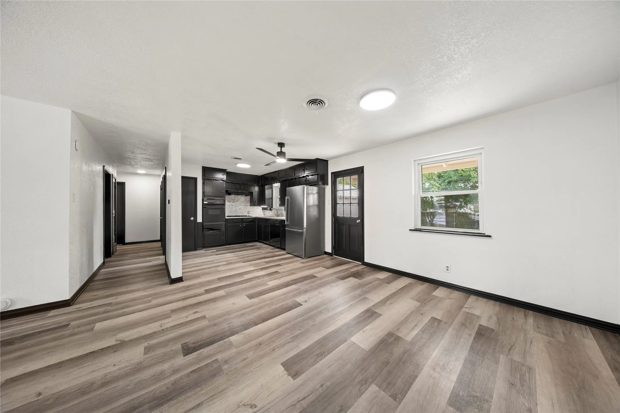 Spacious area featuring wood-finish flooring, a kitchen with black cabinetry and stainless steel appliances, and a ceiling fan