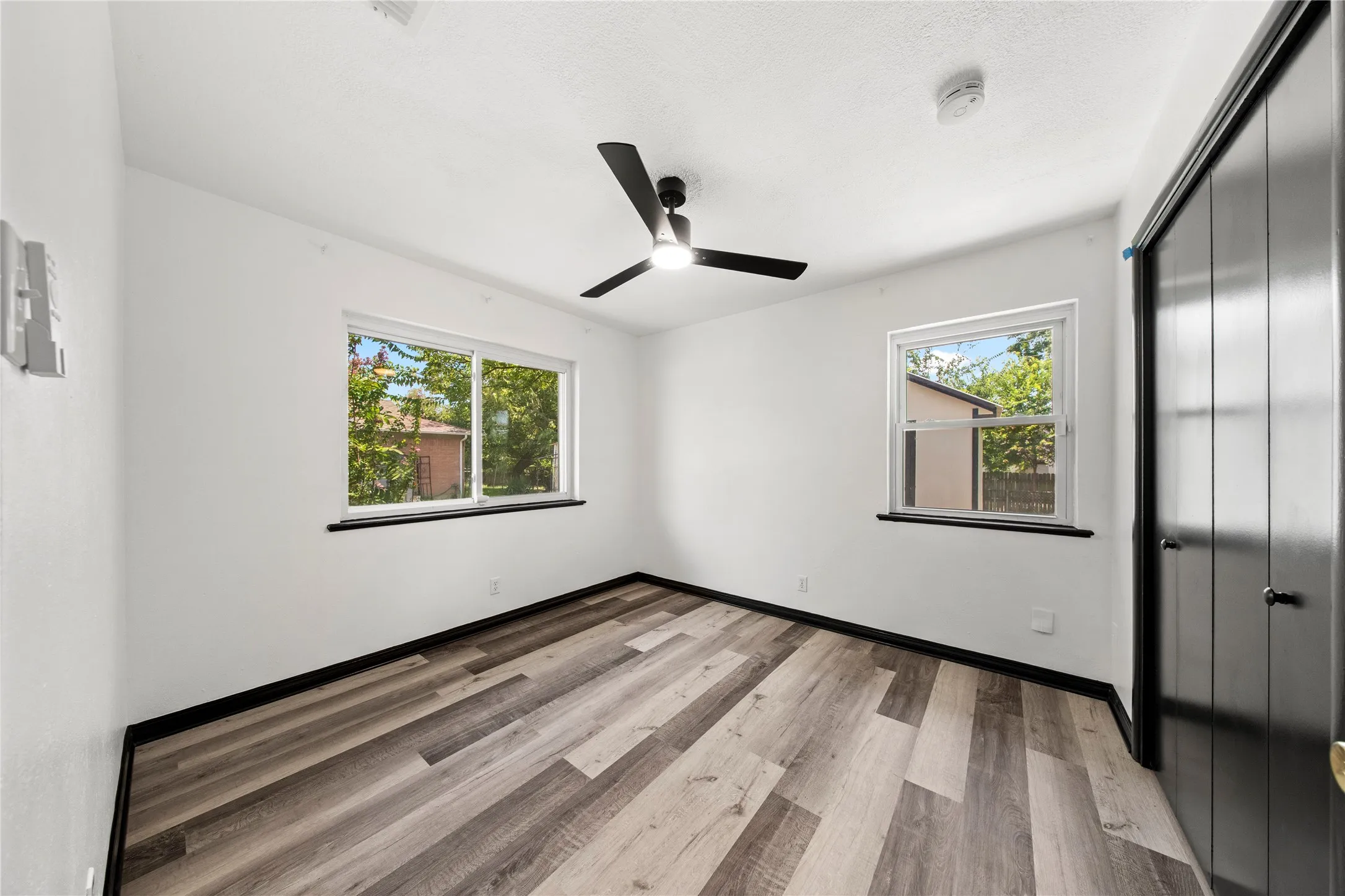 Spacious room featuring wood-finish flooring, two windows, a ceiling fan, and bi-fold closet doors