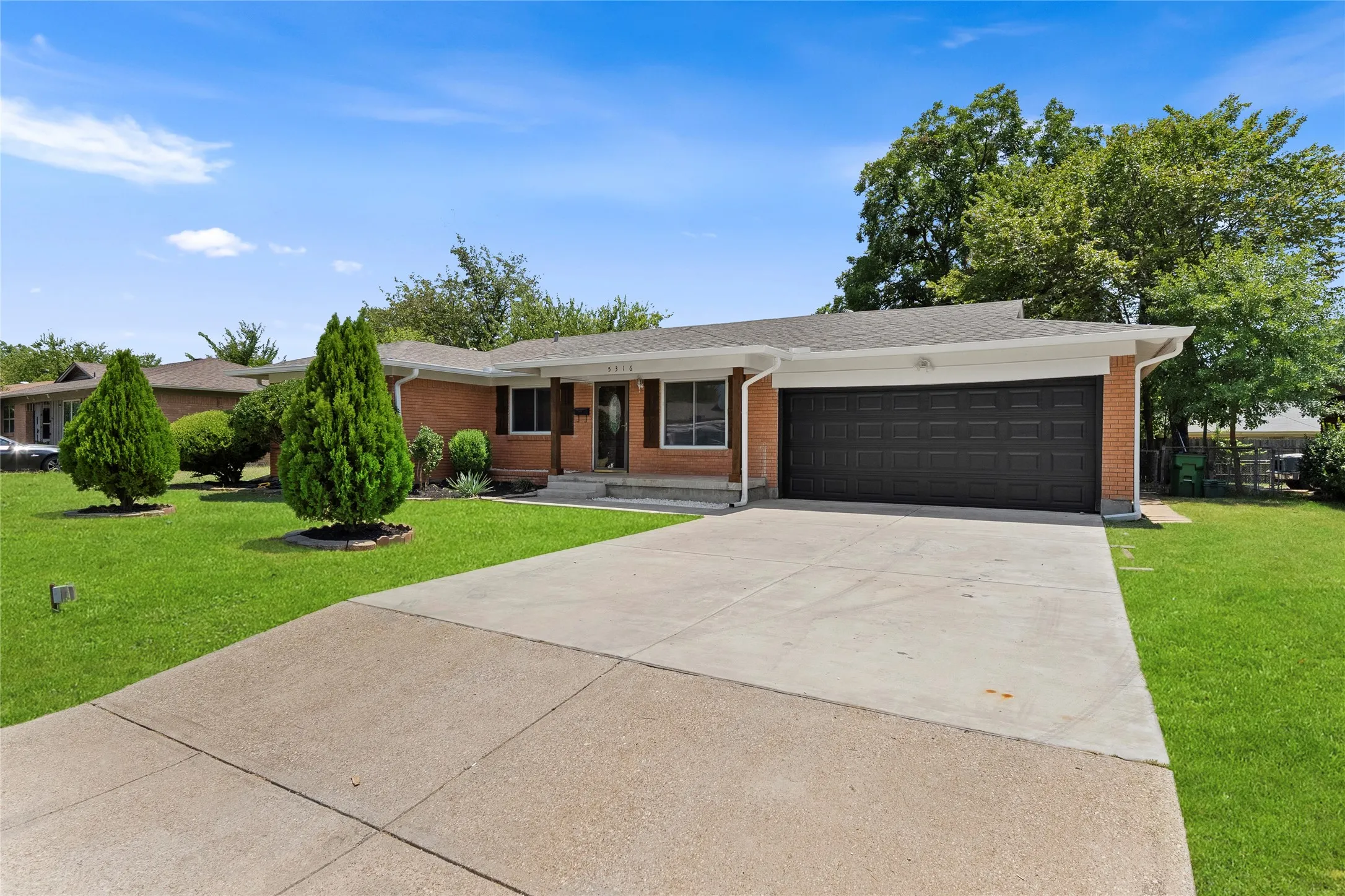 Brick exterior with an attached garage, concrete driveway, and a front lawn with mature landscaping