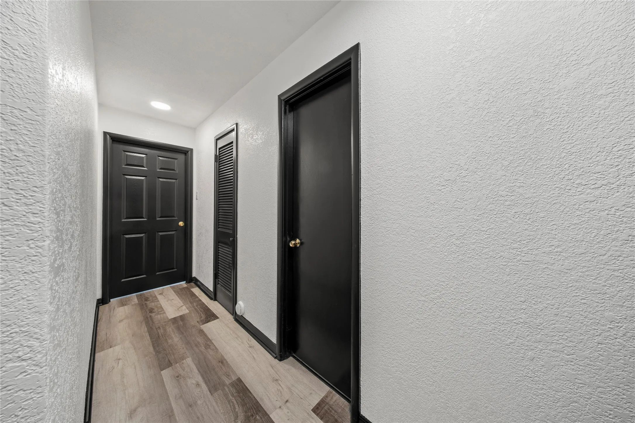 Hallway featuring wood-finish flooring, recessed lighting, and contrasting dark-paneled doors with trim