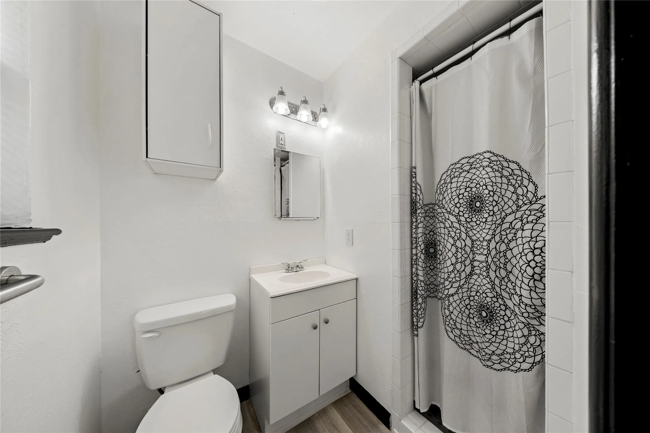 Bathroom featuring a white vanity with a single basin, wall-mounted medicine cabinet, modern light fixture, and a tiled shower enclosure