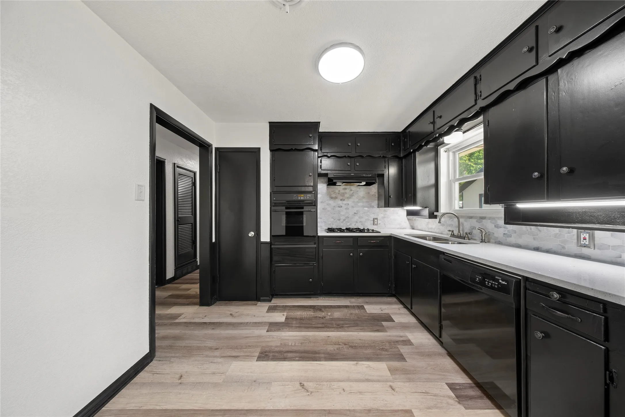 Kitchen featuring dark cabinetry, light countertops, a tile backsplash, wood-finish flooring, and a built-in oven