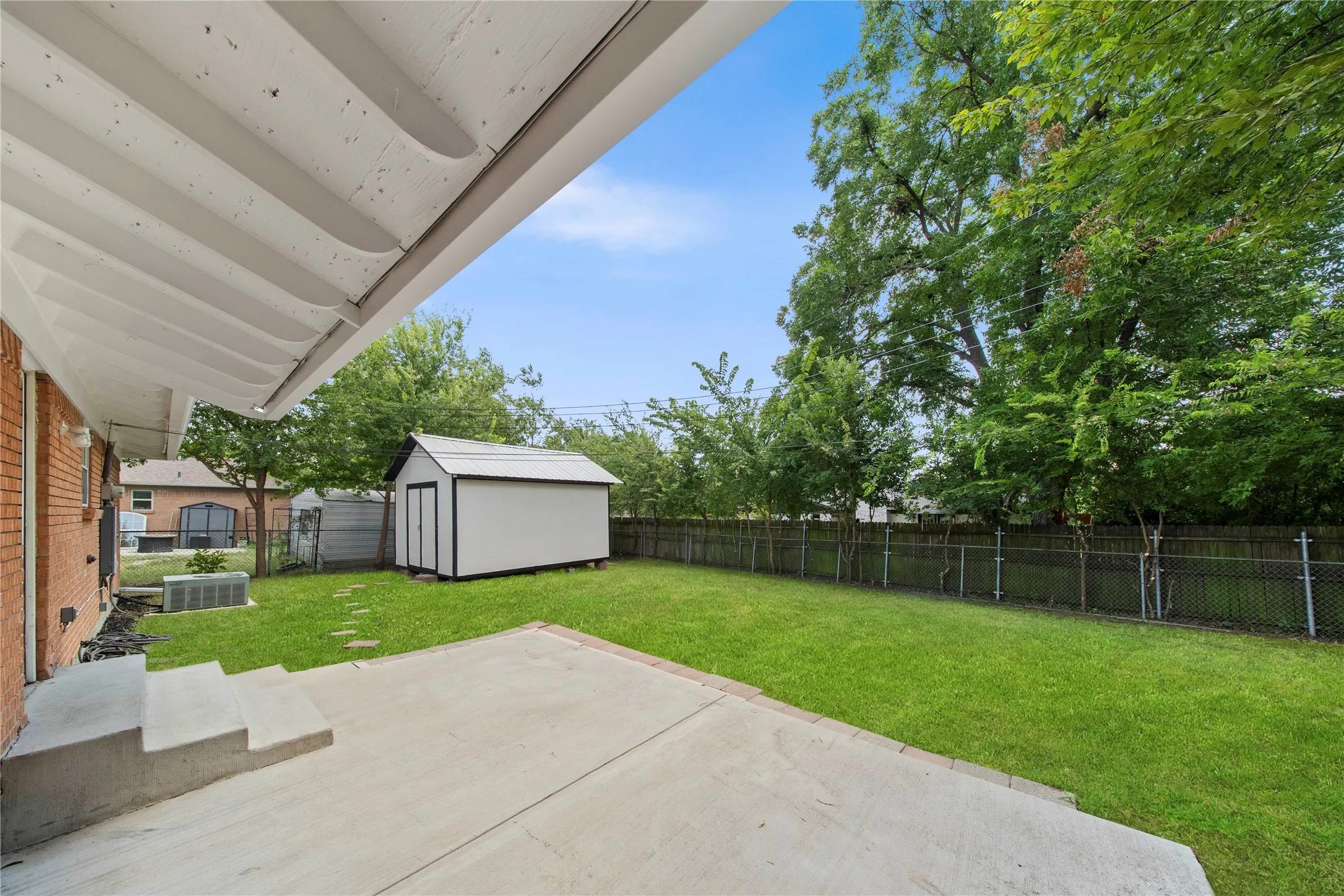 Expansive backyard featuring a manicured lawn, concrete patio, and a storage shed