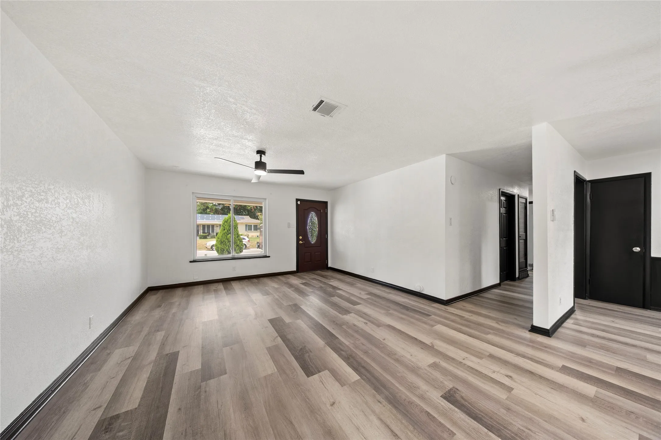 Spacious room featuring wood-finish flooring, a contemporary ceiling fan, and a paneled entry door with an oval glass insert