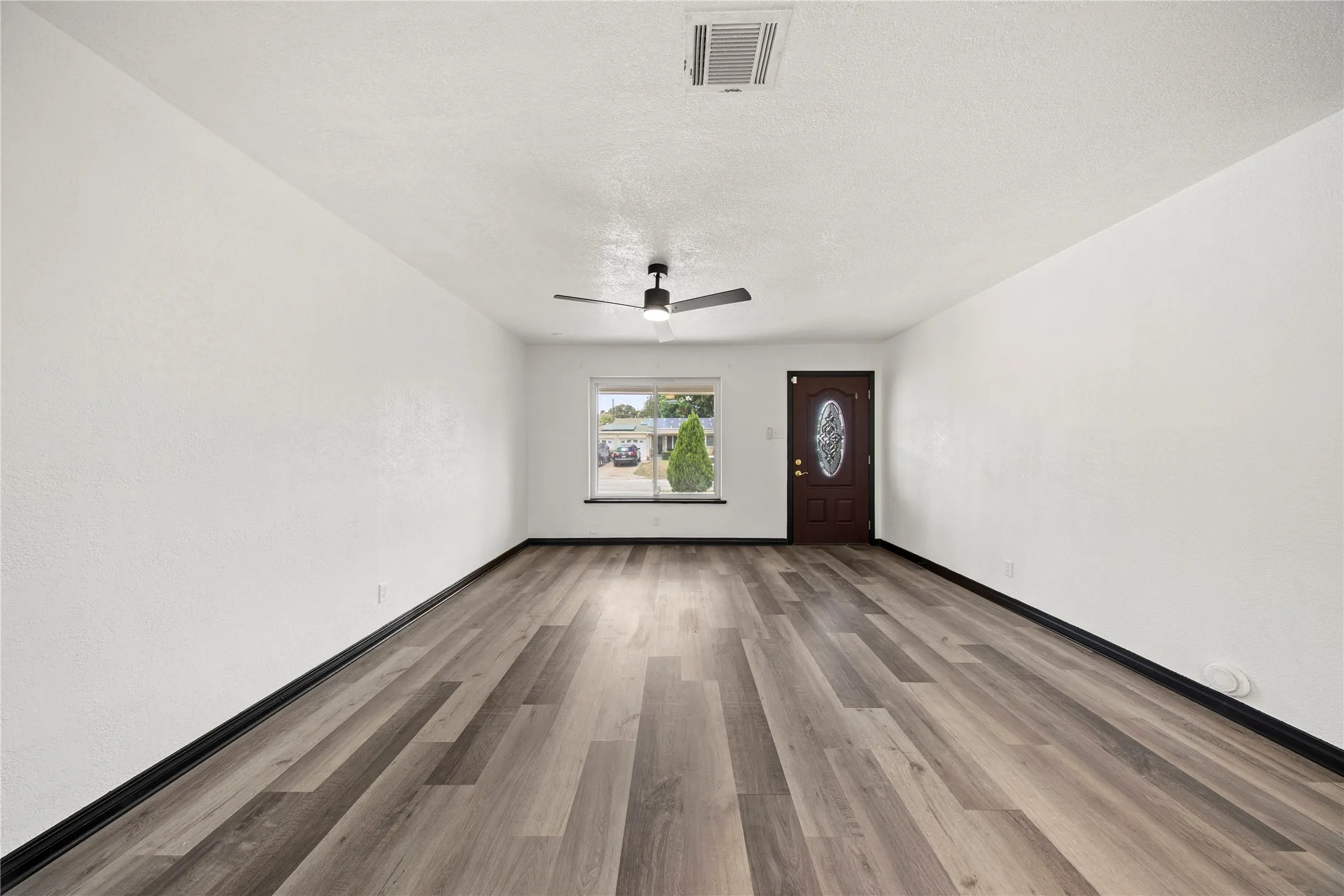 Spacious interior featuring wood-finish flooring, a dark wood-paneled door with an oval glass insert, and a ceiling fan with integrated lighting