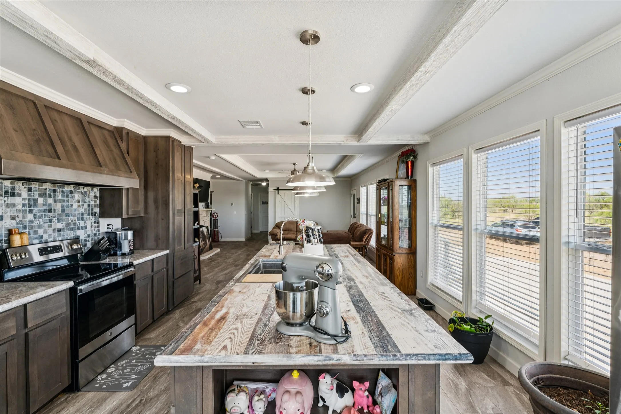 Kitchen featuring a large center island with a wood-finish countertop, dark wood-finish cabinetry, stainless steel range, mosaic tile backsplash, and multiple windows
