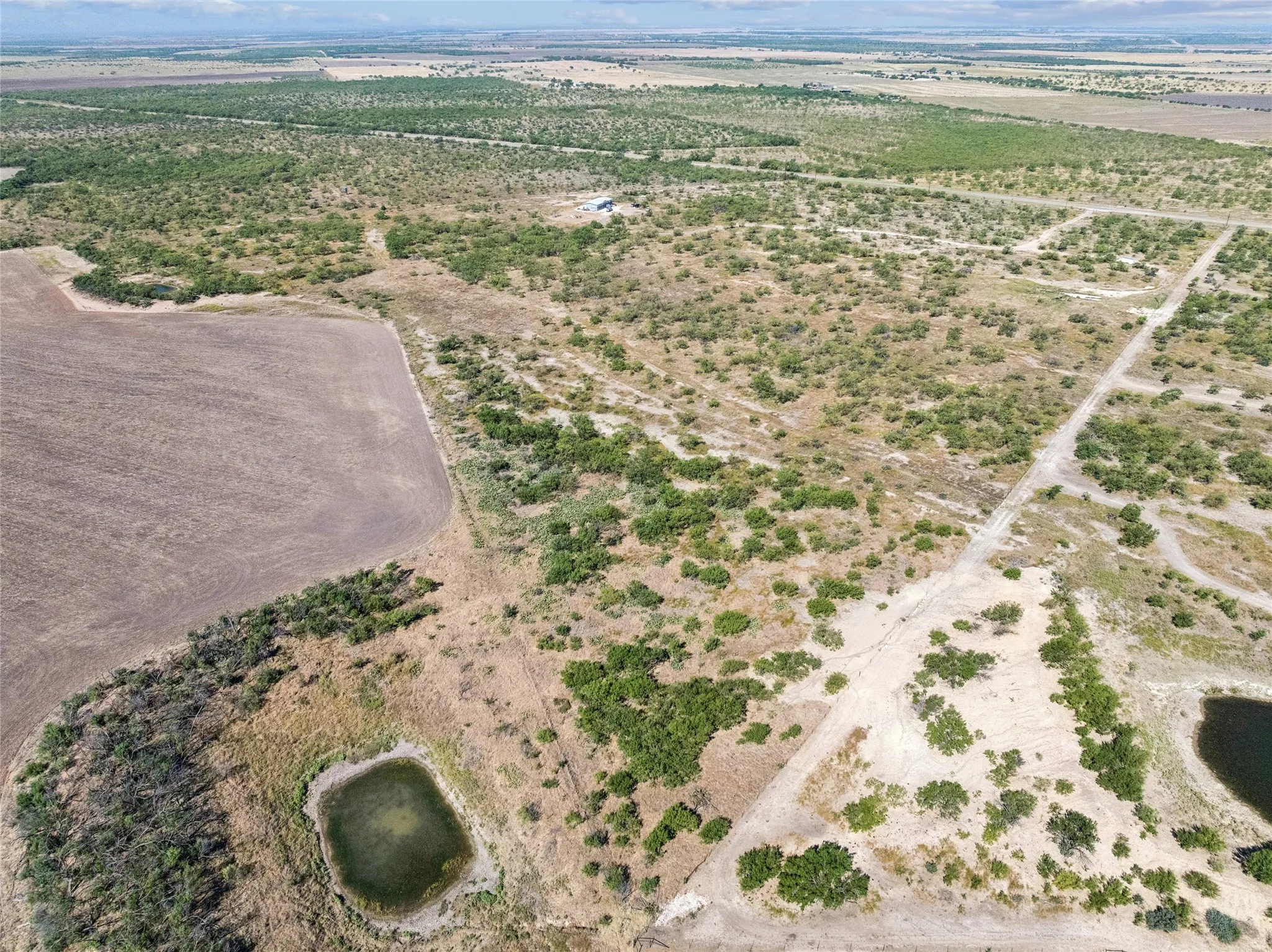 Expansive rural acreage with varied terrain, featuring two distinct water bodies, a section of tilled land, and scattered natural vegetation