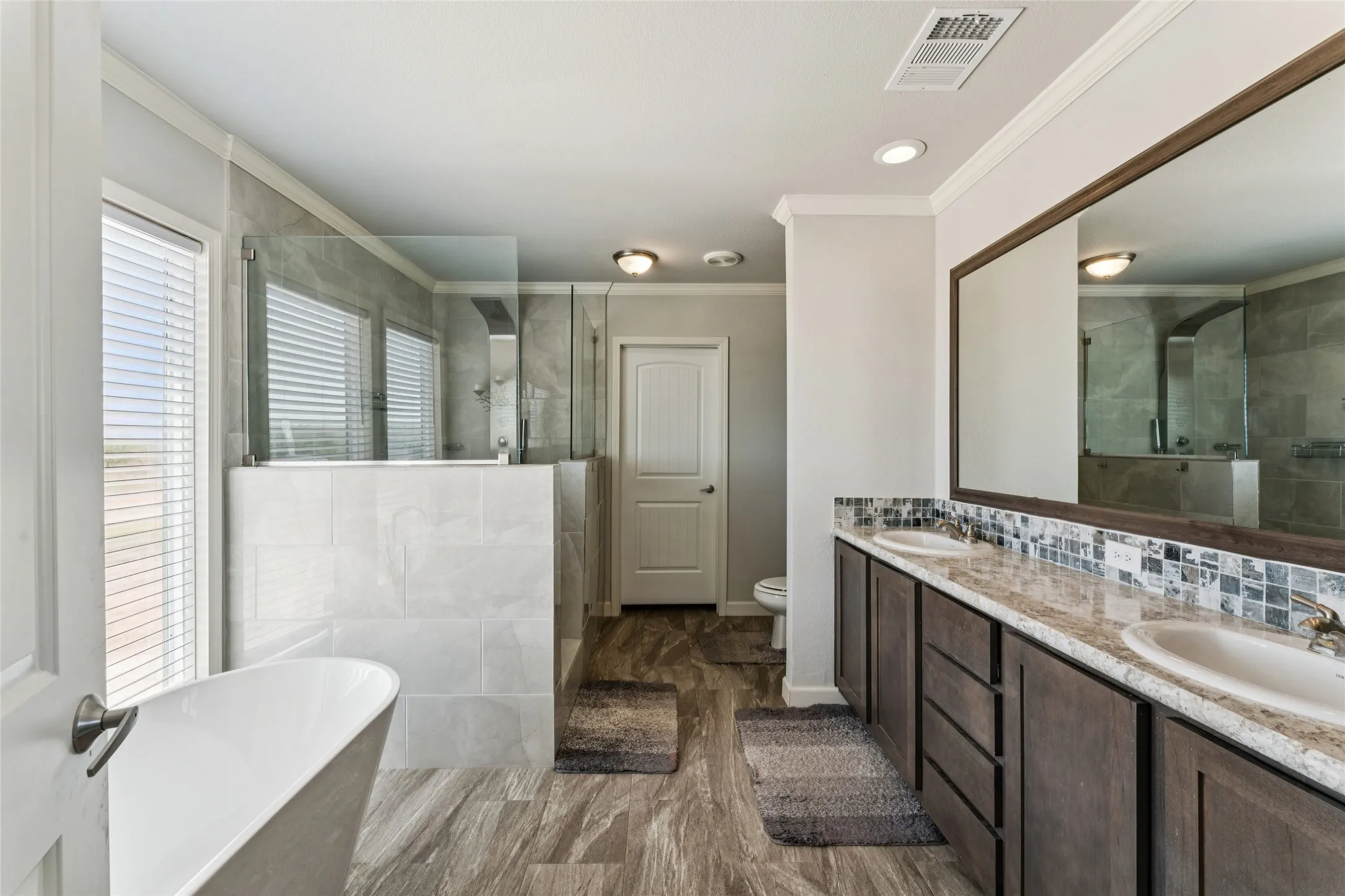 Primary bathroom with freestanding soaking tub, walk-in shower with glass enclosure, dual vanity with undermount sinks, wood-finish cabinetry, and vinyl plank flooring