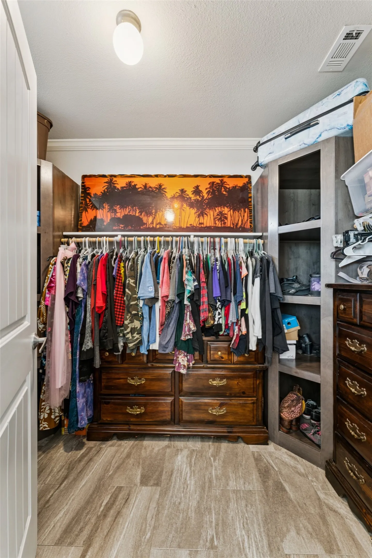 Primary walk in closet with built in shelving vinyl plank flooring, and crown molding