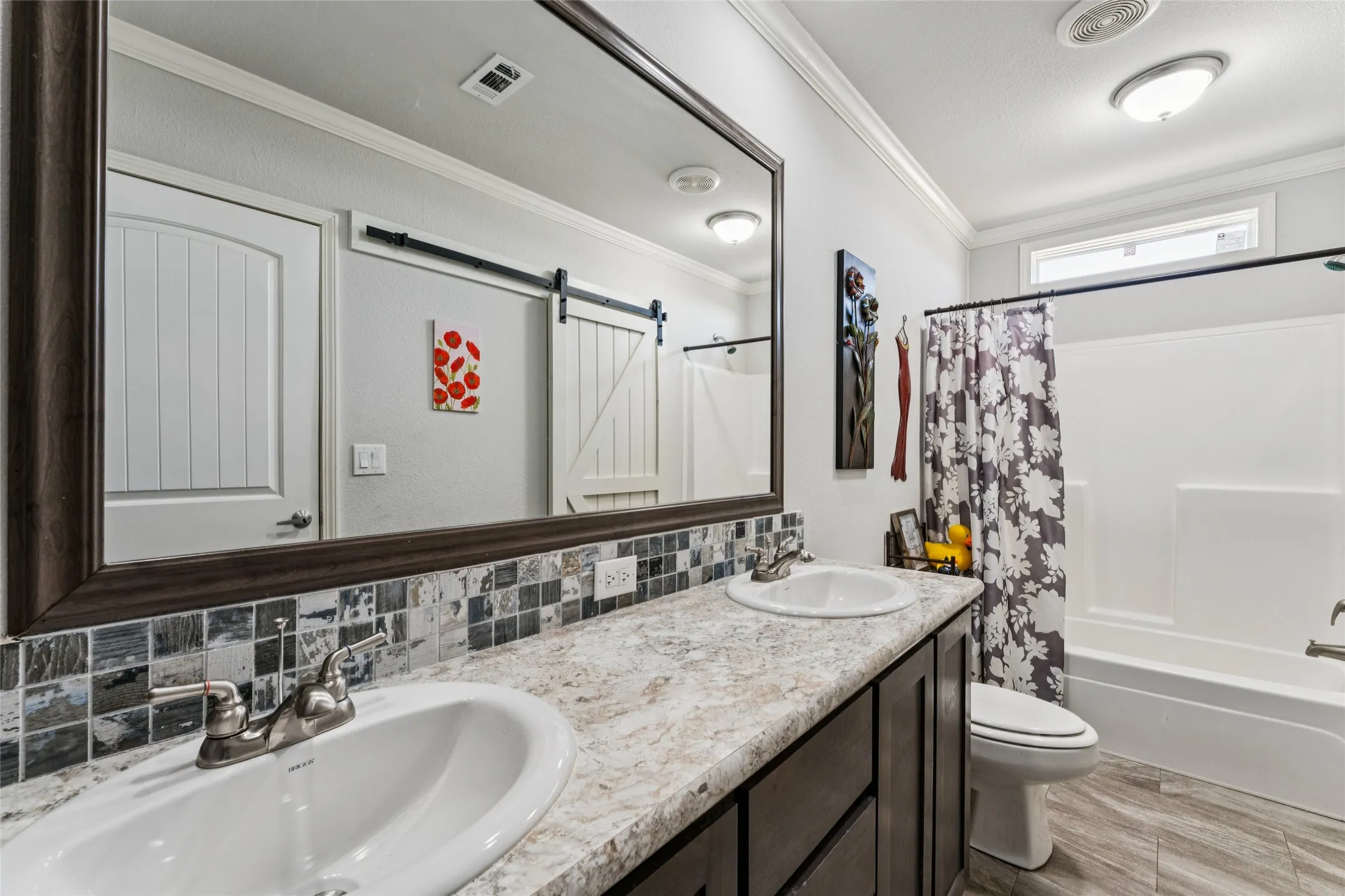 Secondary bathroom with double vanity with undermount sinks, mosaic tile backsplash, a framed mirror, and an oversized linen closet