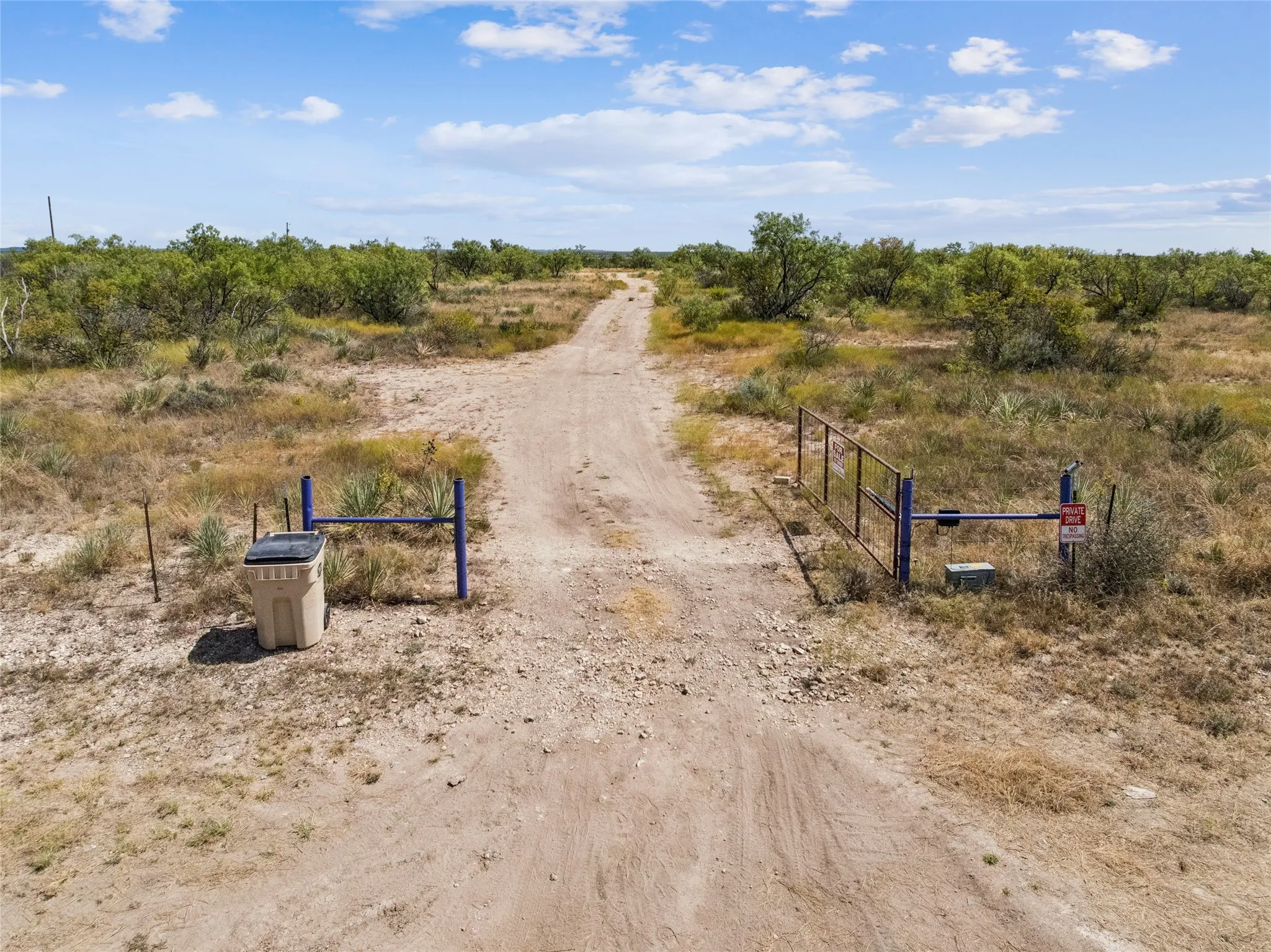 Gated entrance with a dirt driveway extending through the natural vegetation to the home