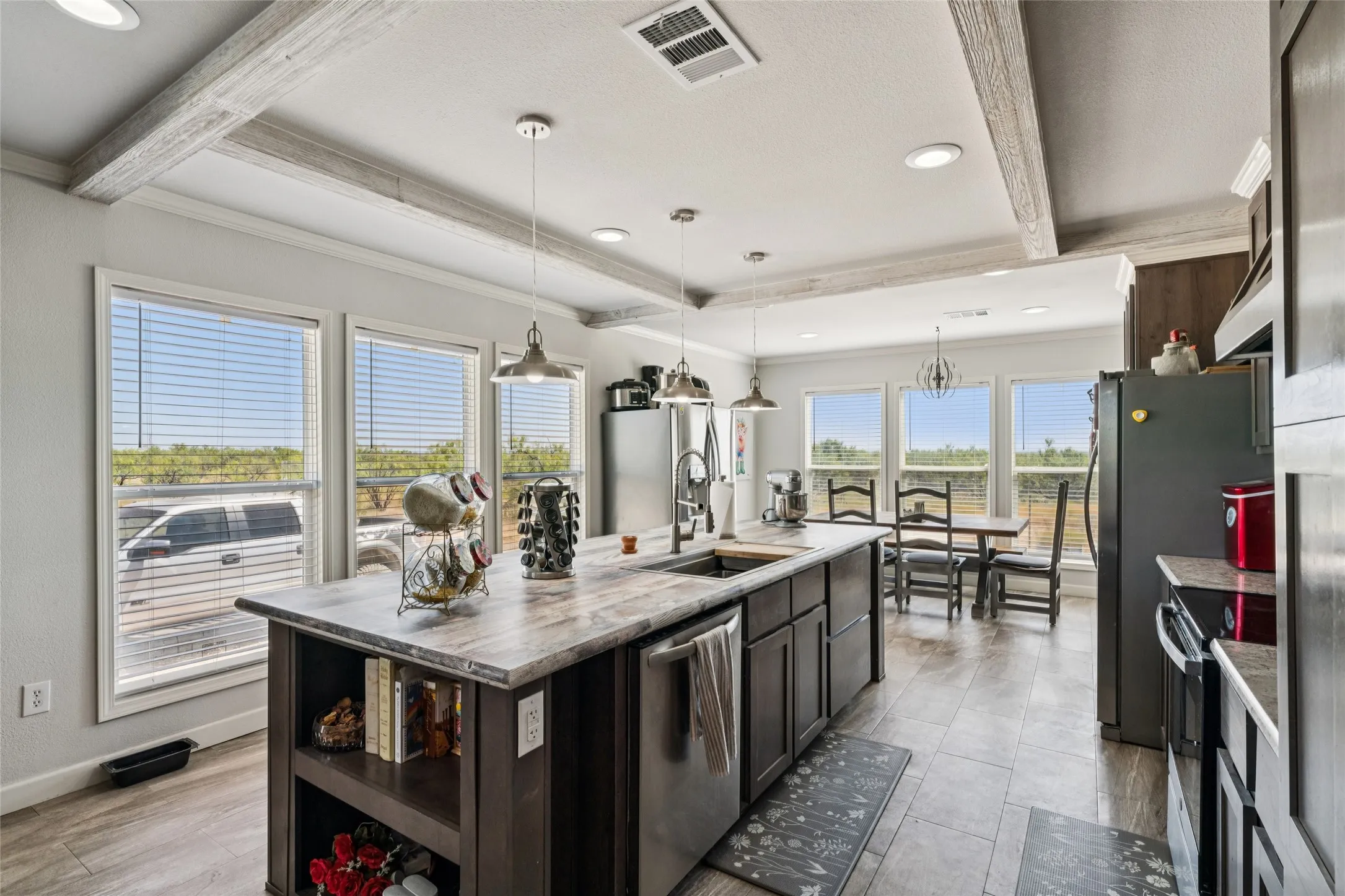 Kitchen with exposed wood-finish beams, recessed lighting, central island with integrated sink, stainless steel appliances, and vinyl plank flooring