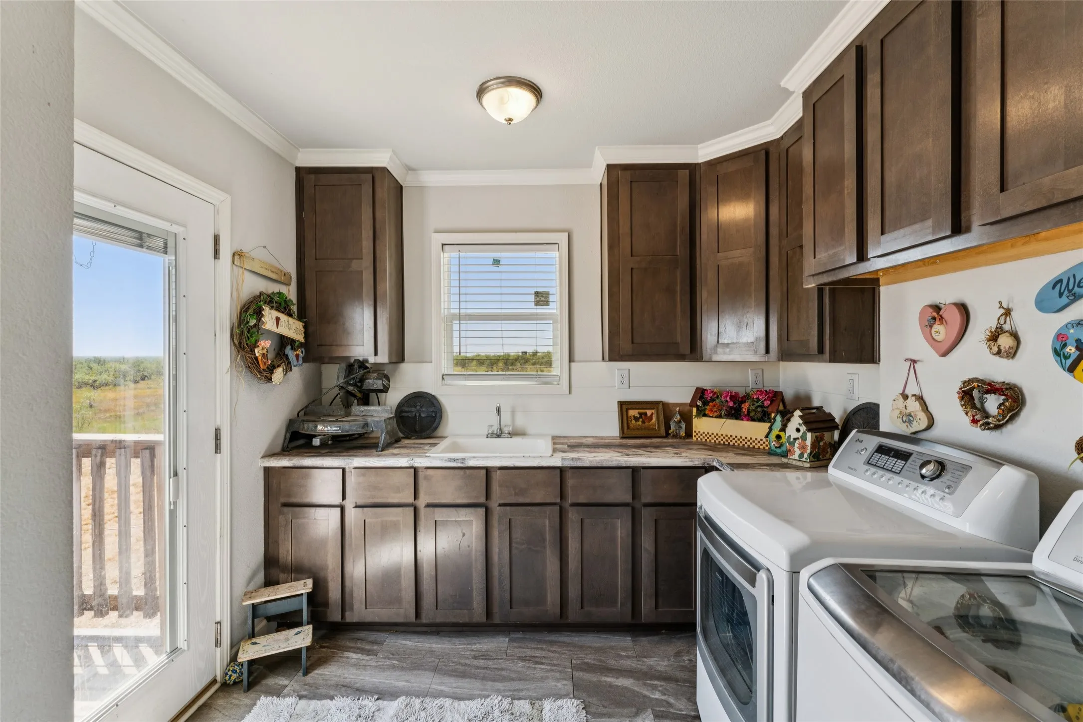 Wood-finish cabinetry with crown molding, light-toned countertops, vinyl plank and a white sink basin with full washer and dryer hookups