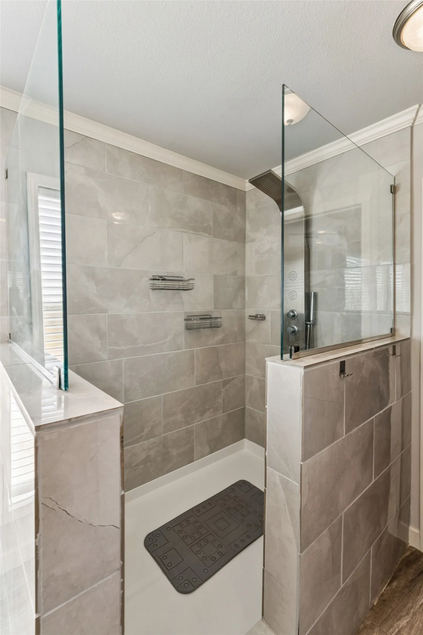 Walk-in shower with full-height tile walls, glass panels, a rain shower head, and built-in shelving
