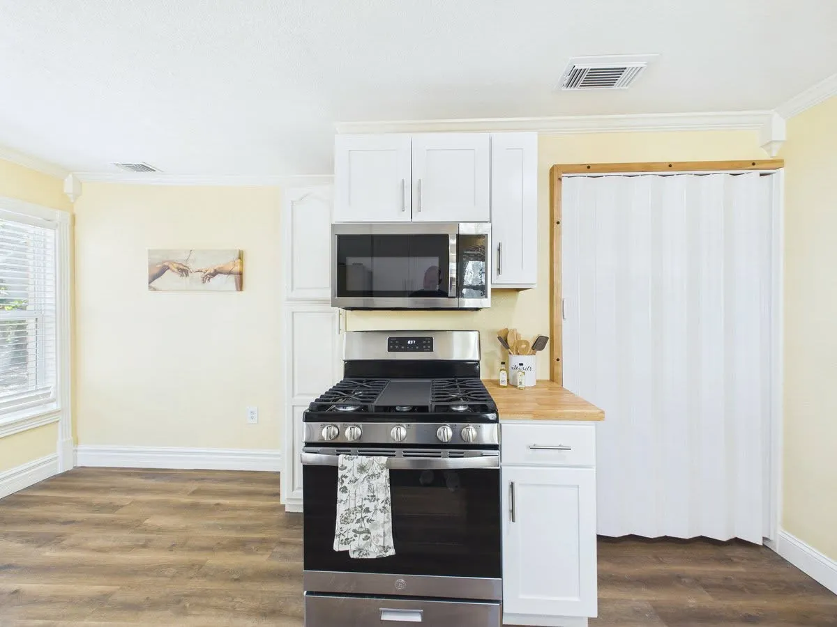 Stainless steel range with an overhead microwave, white upper and lower cabinetry, wood-finish flooring, and crown molding