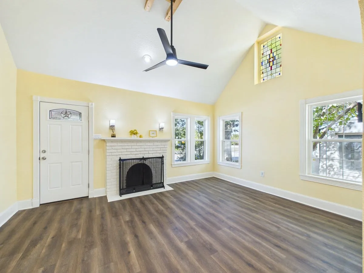 Spacious interior featuring a vaulted ceiling, wood-finish flooring, white brick fireplace, and multiple windows