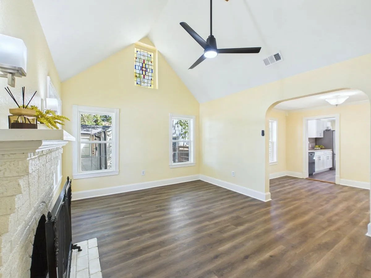 Vaulted ceiling with a stained-glass window, wood-finish flooring, a painted brick fireplace, and a modern ceiling fan