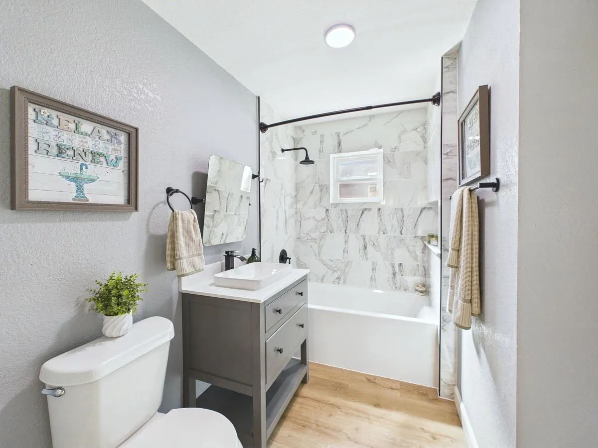 Bathroom featuring a white bathtub, marble-look tile surround, dark gray vanity with a vessel sink, and wood-finish flooring