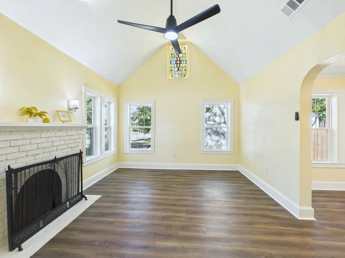 Vaulted ceiling, wood-finish flooring, white brick fireplace, stained glass window, and an arched doorway