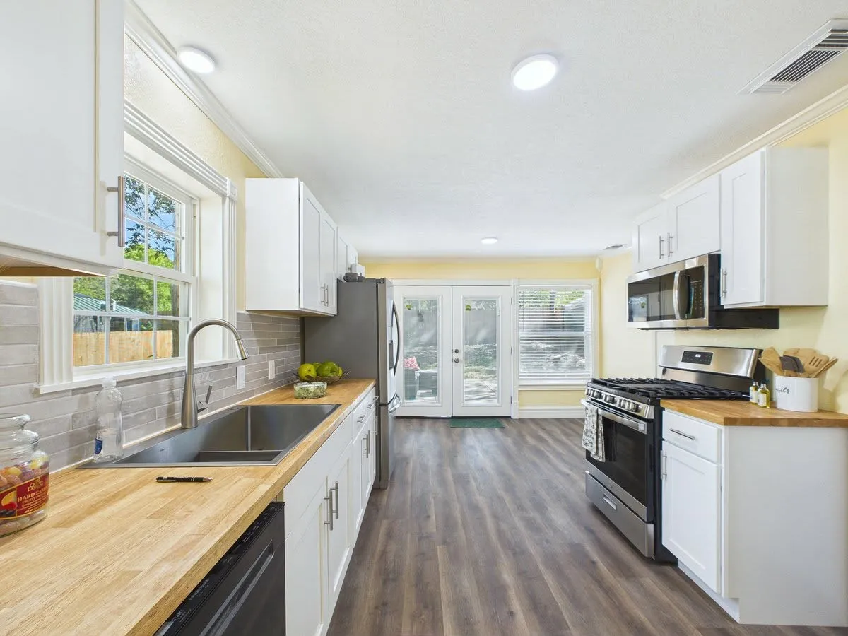 Galley kitchen featuring wood-finish countertops, white cabinetry, stainless steel appliances, and wood-finish flooring