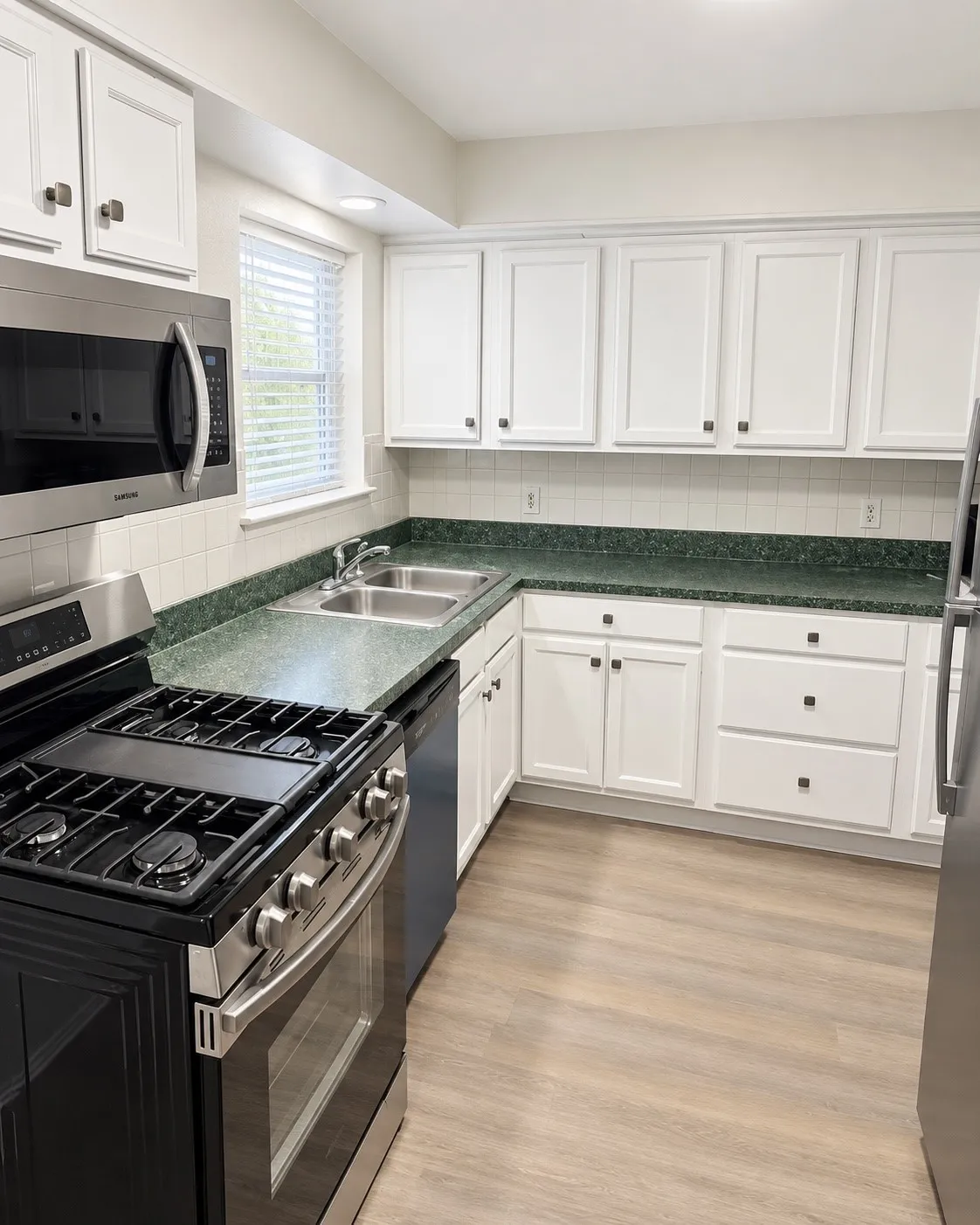 White cabinetry with square pull hardware, green speckled countertops, stainless steel microwave, gas range, and wood-finish flooring