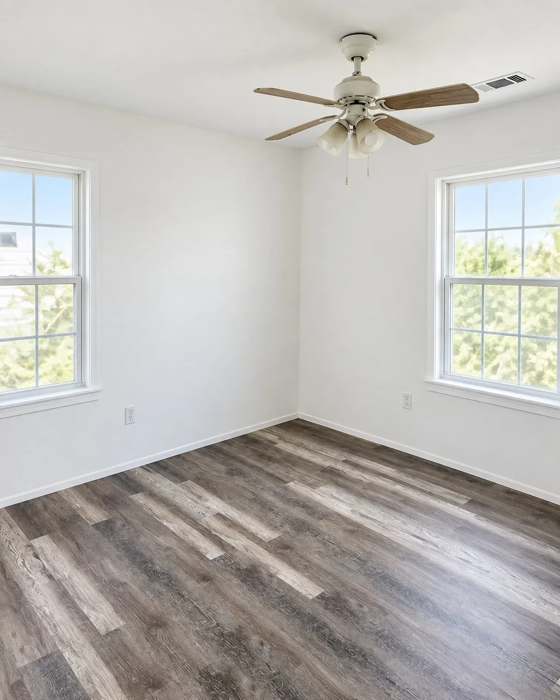 Bright interior with two double-hung windows, a ceiling fan with light fixture, and wood-finish flooring